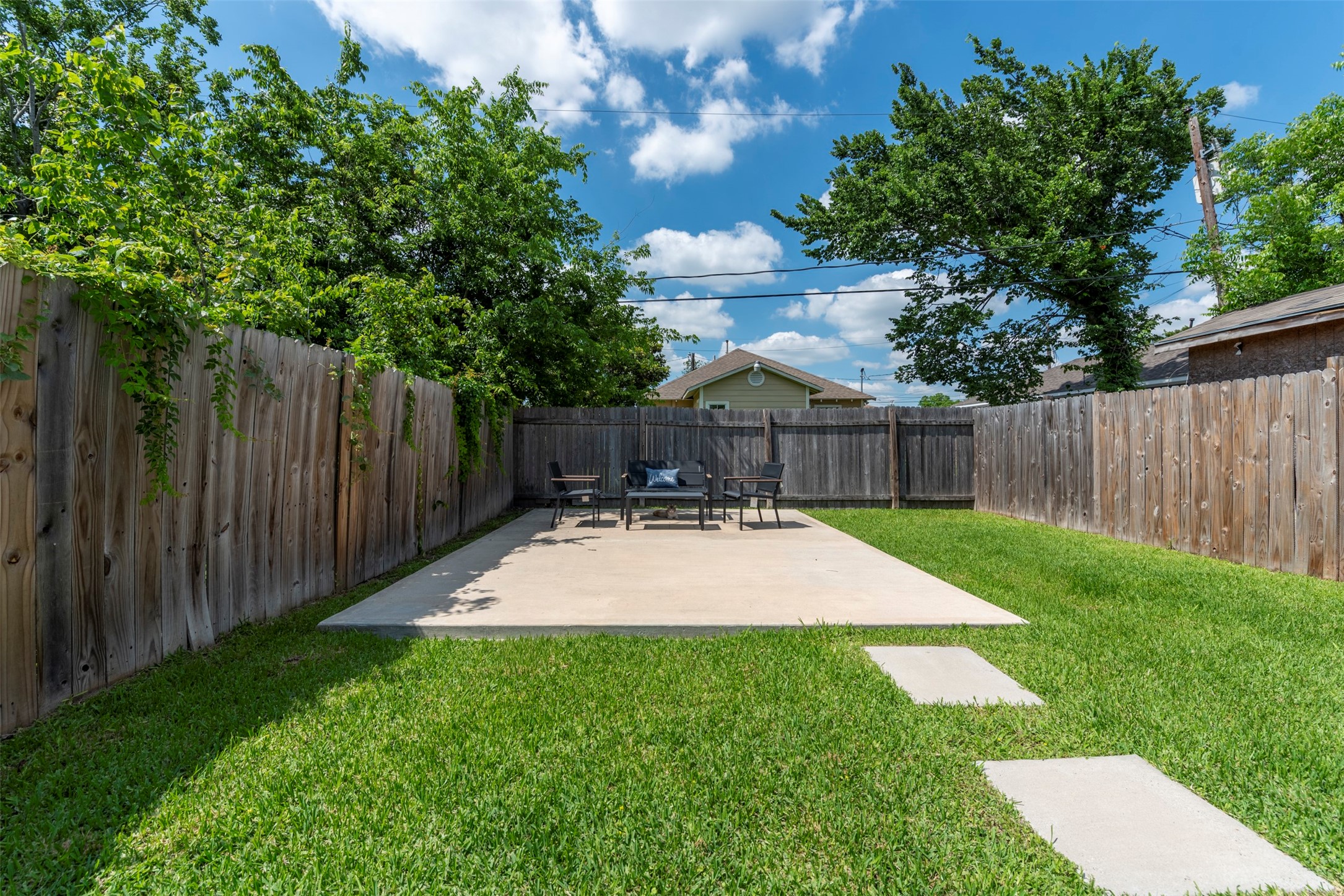 Spacious fully fenced backyard with a large poured concrete patio, mature shade trees, manicured lawn, and privacy wood fence on all three sides.