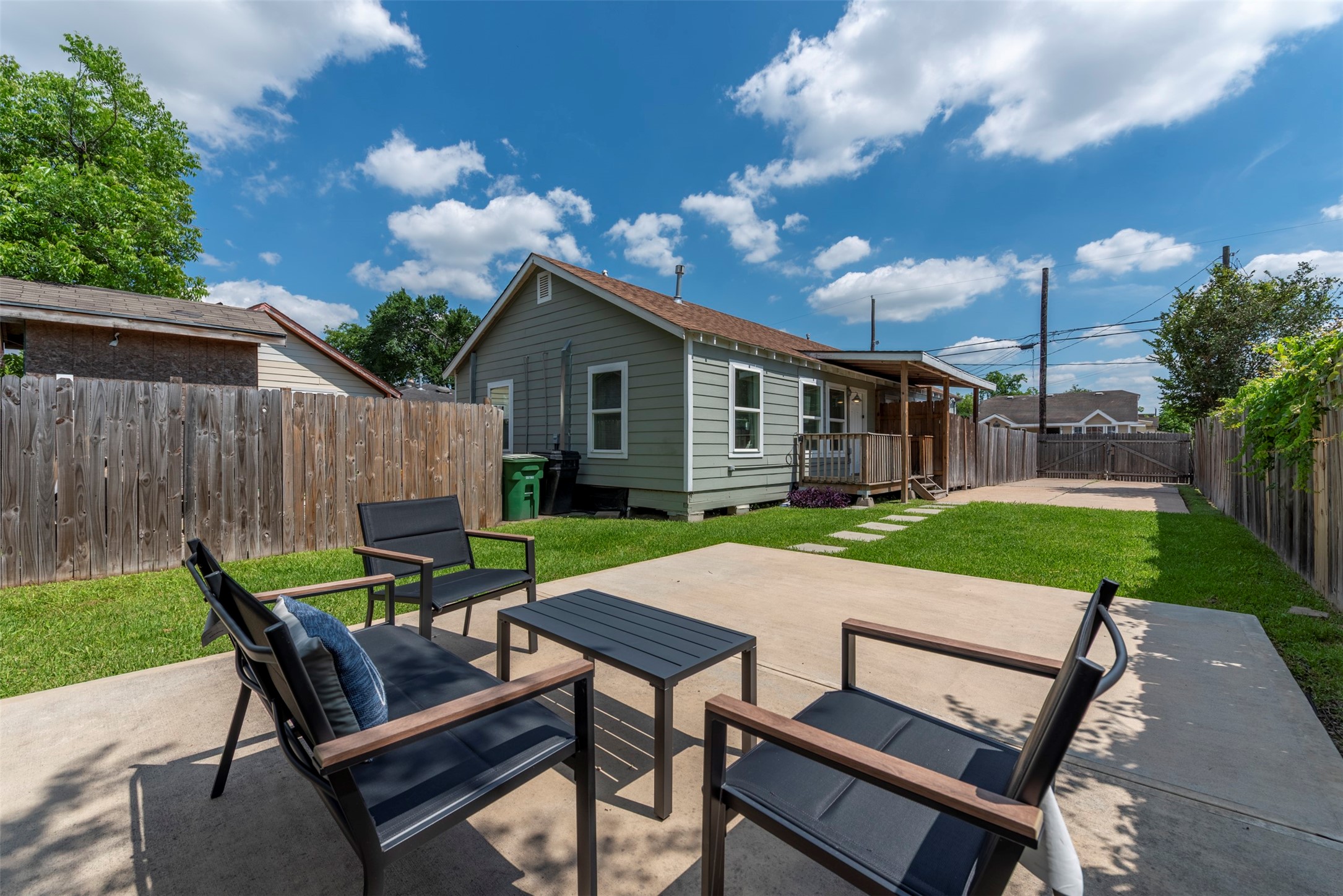 Backyard entertaining area with poured concrete patio, modern outdoor seating, manicured lawn, concrete stepping stone path, and covered back porch with wood beam detailing.