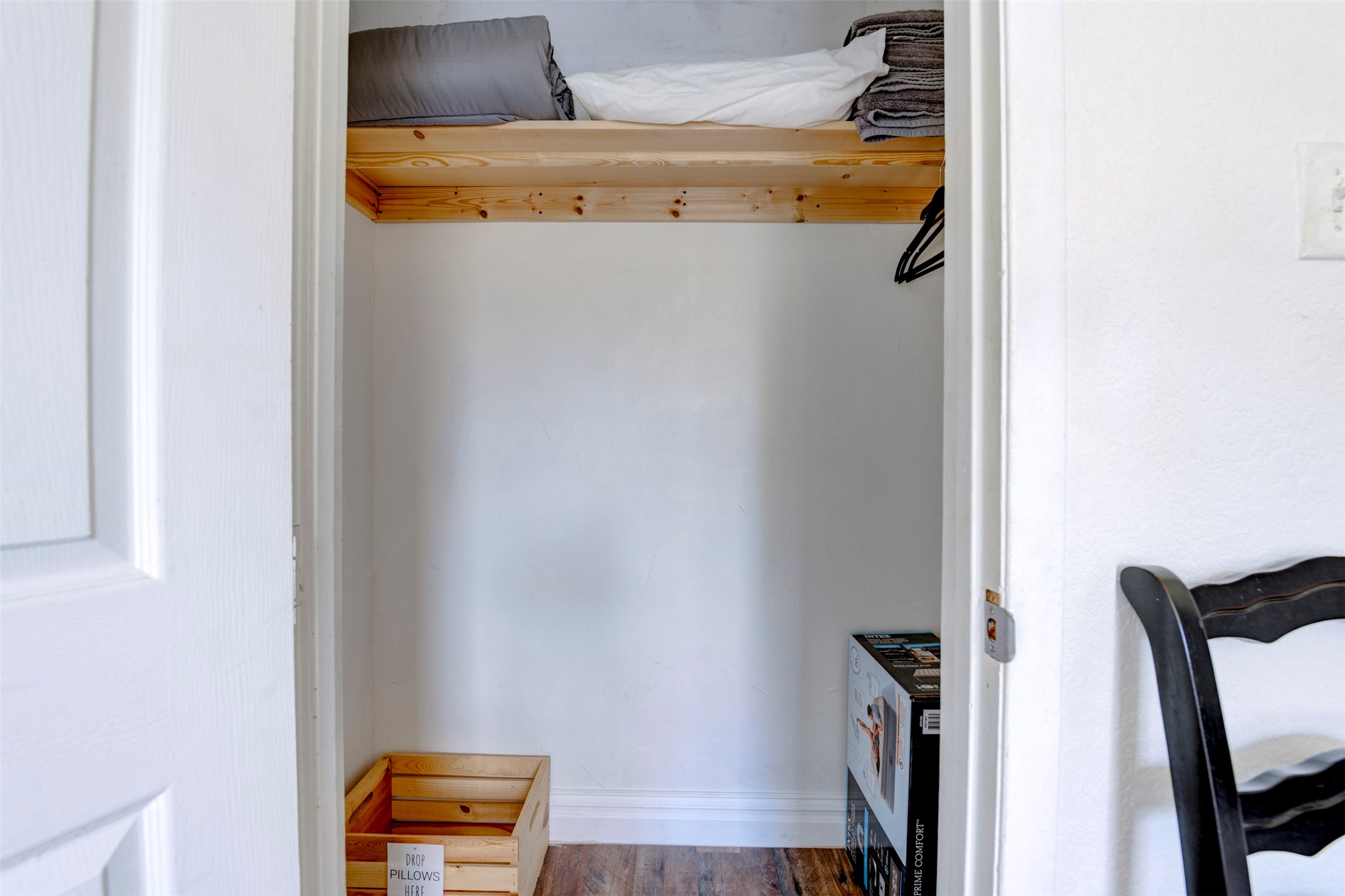 Spacious closet with natural pine wood upper shelf, hanging rod, freshly painted white walls, and wood-look flooring throughout.