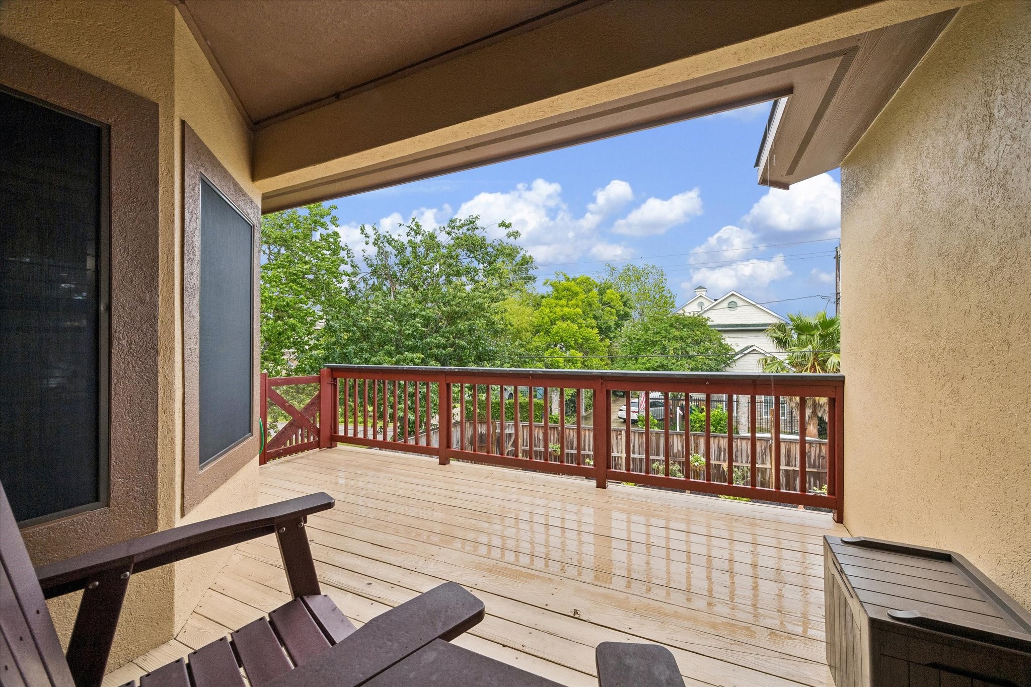 Spacious covered upper deck with wood flooring and railing, offering elevated views of the backyard and surrounding greenery. Ideal for outdoor seating, dining, or relaxing with direct access to the main living area.