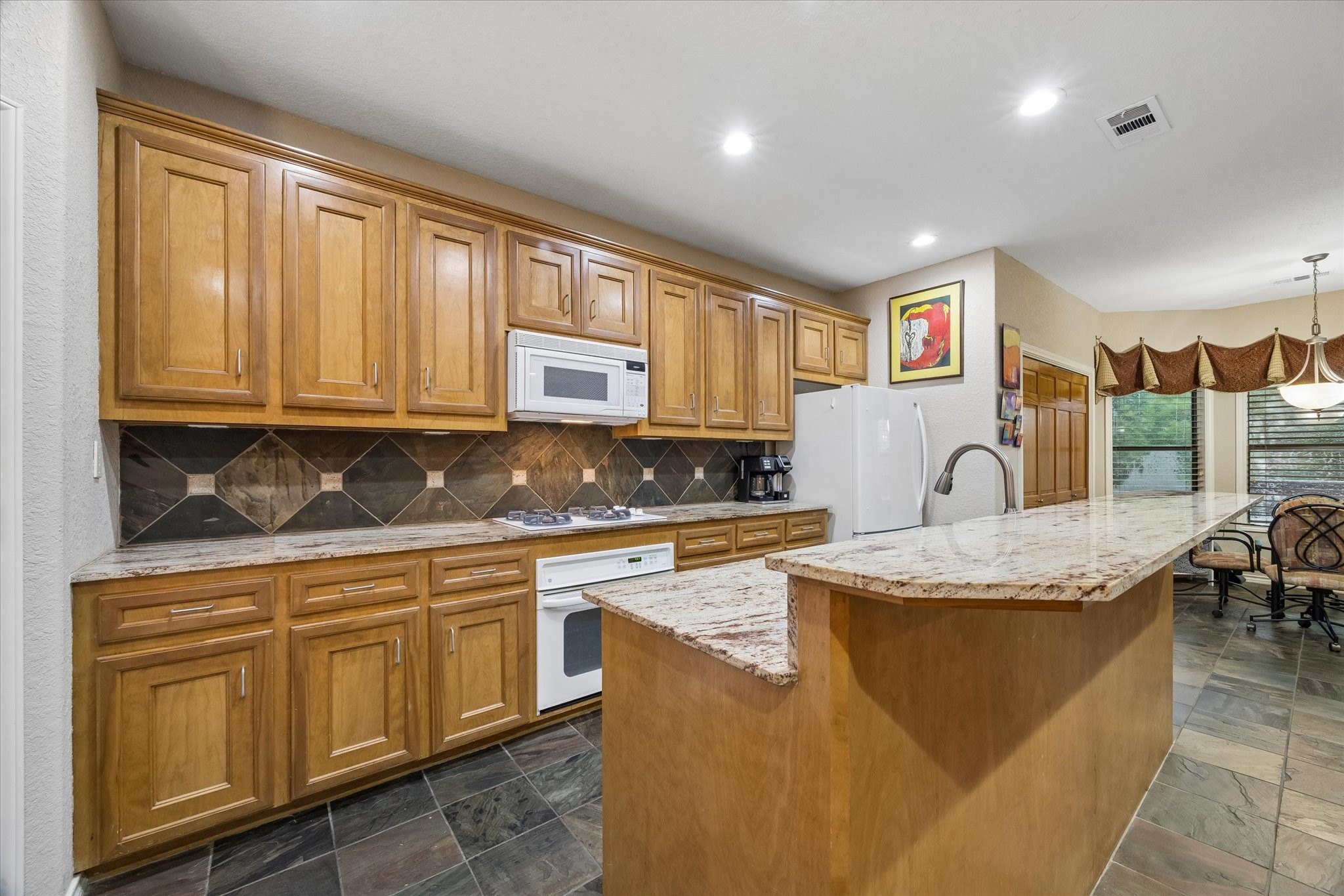 Kitchen featuring extensive cabinetry, granite countertops, and tile backsplash. Functional layout with ample prep space, built-in appliances, and center island for additional workspace. Kitchen featuring extensive cabinetry, granite countertops, and tile backsplash. Functional layout with ample prep space, built-in appliances, and center island for additional workspace.
