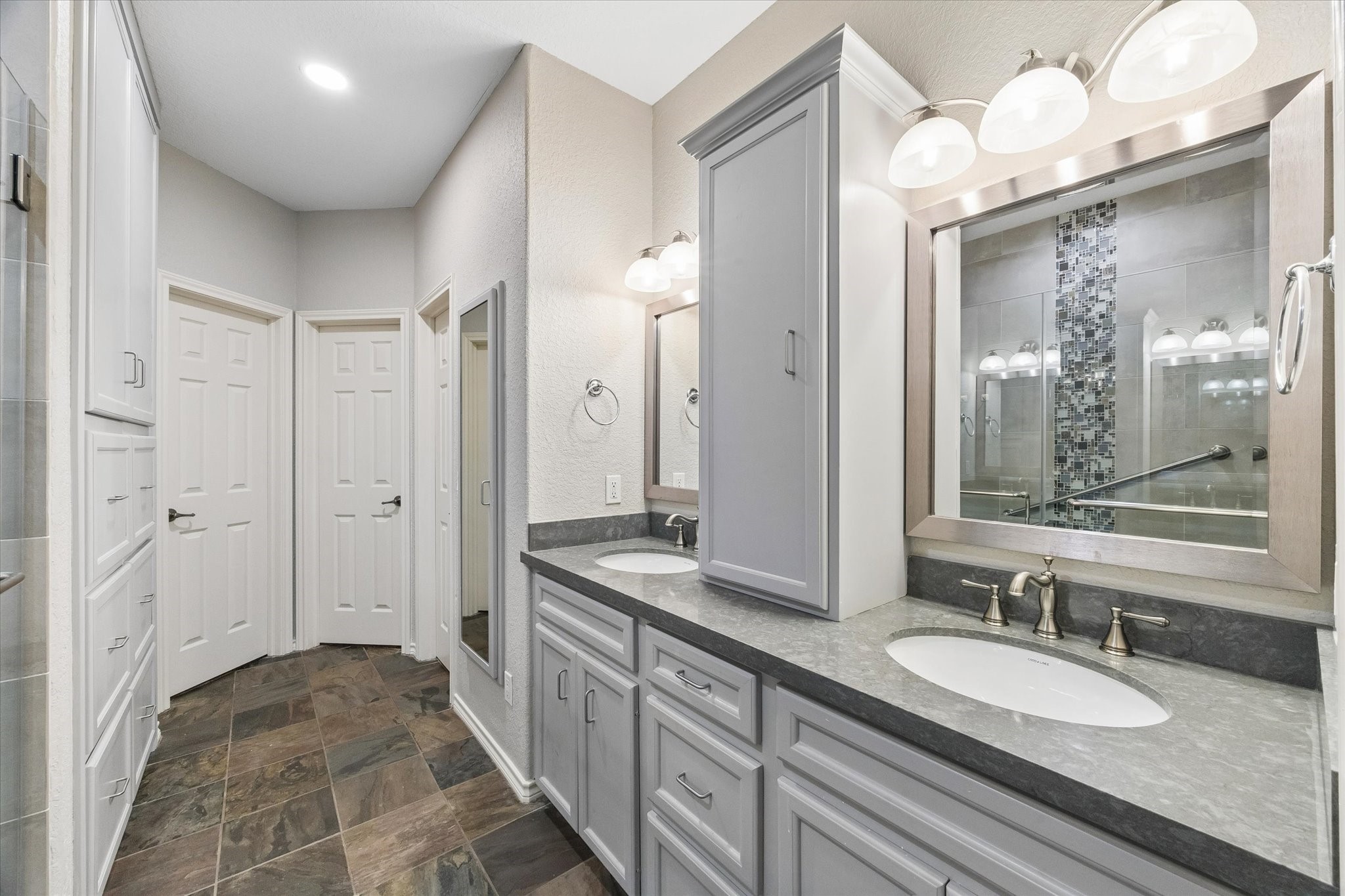 Primary bathroom with dual vanities, updated cabinetry, and ample storage. Walk-in shower with tile surround and glass enclosure provides a clean, modern finish. Two walk-in closets and a bonus space currently called the "snore" room but can be used for multiple purposes.