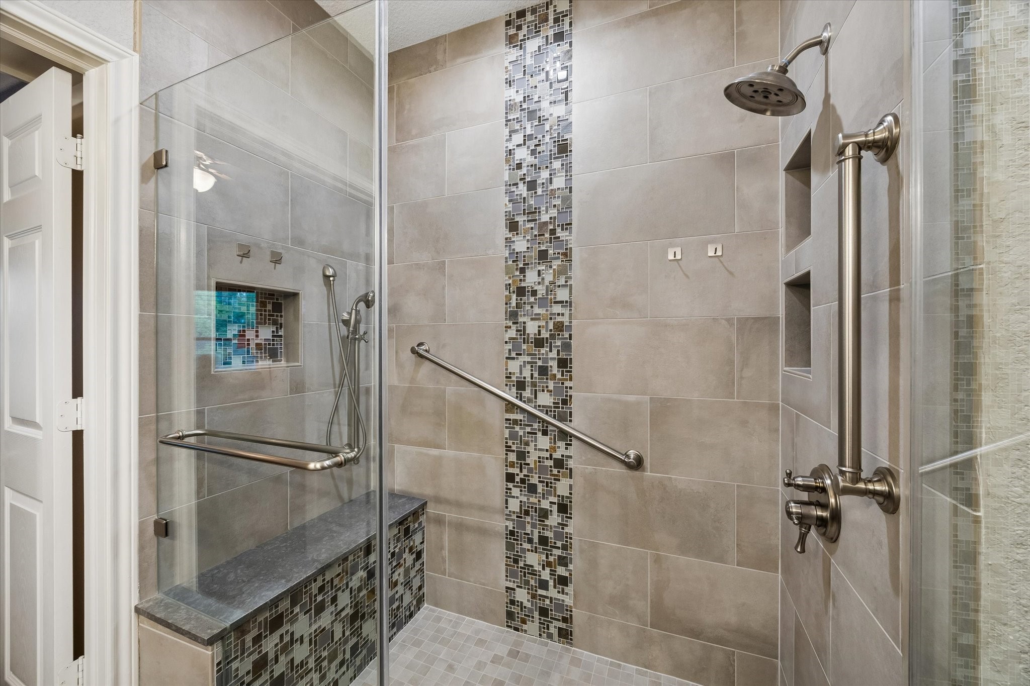 Walk-in shower with glass enclosure, tile surround, and decorative accent strip. Features built-in bench seating, recesses niches, and grab bars for added functionality.