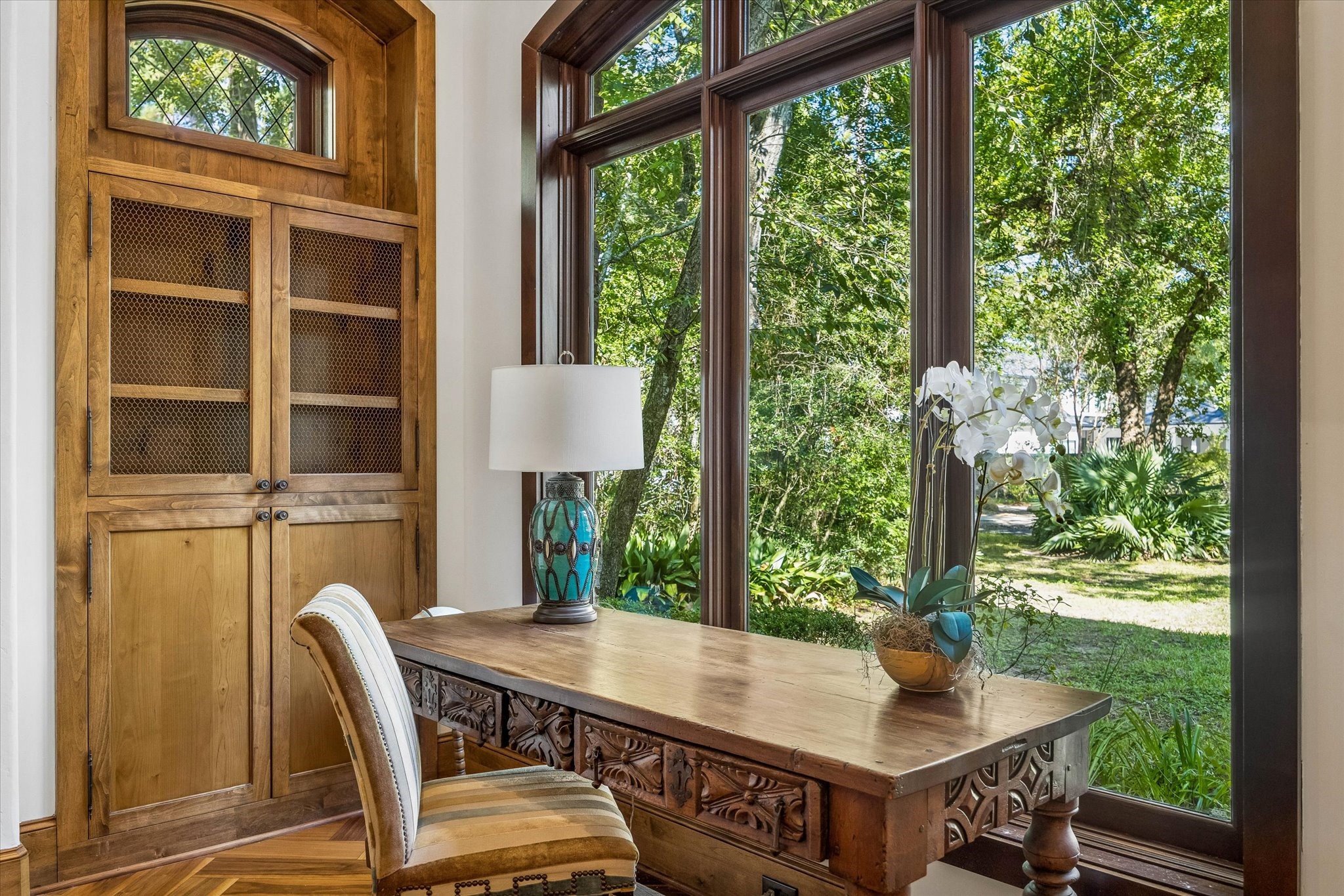 A quiet corner of the living room overlooking the front grounds, where expansive arched windows fill the space with natural light and custom wood cabinetry adds warmth and character.