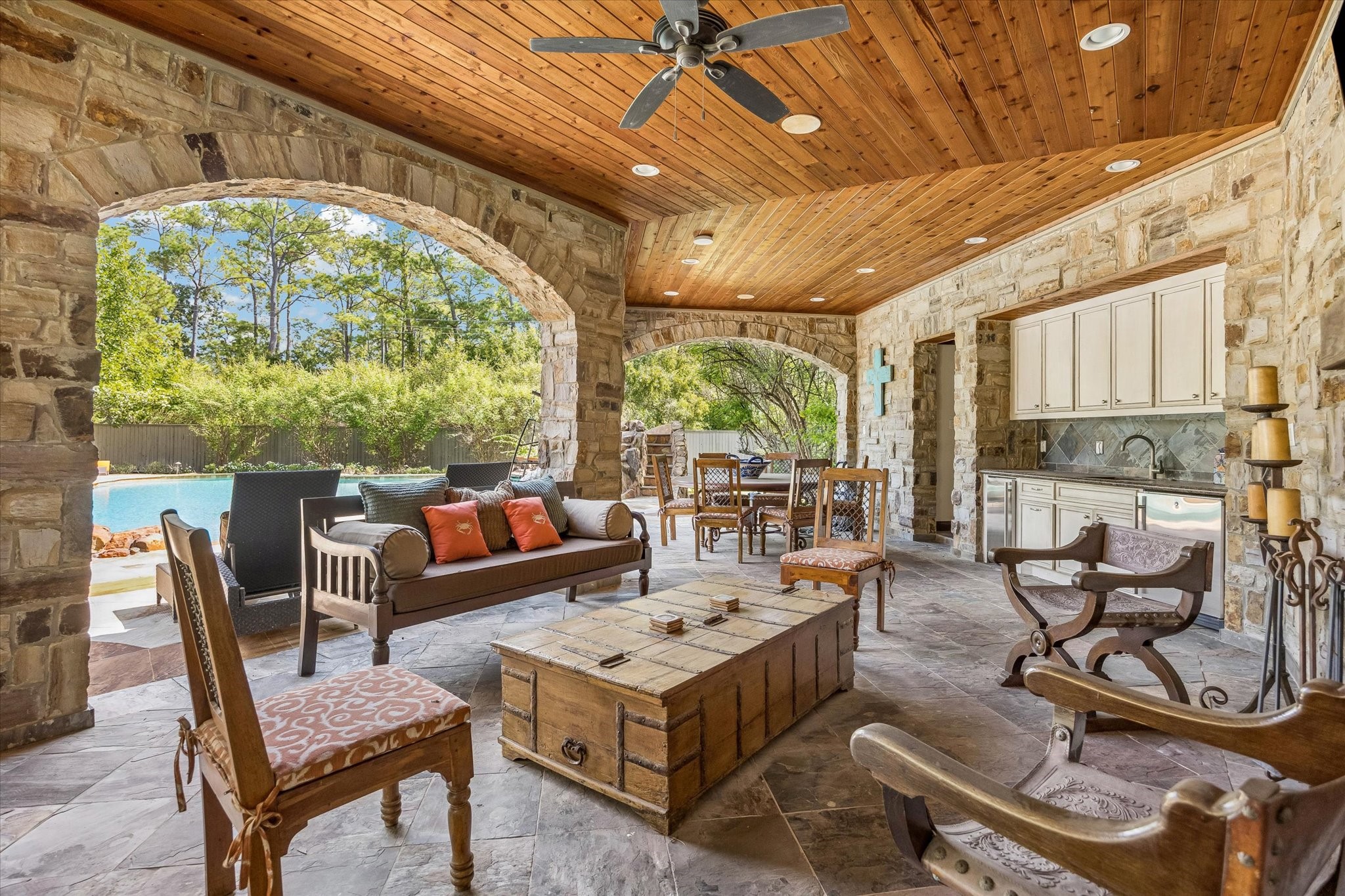 Designed for relaxing and entertaining, the separate pavilion features graceful stone archways, a wood-plank ceiling, and generous covered space for dining and gathering by the pool.