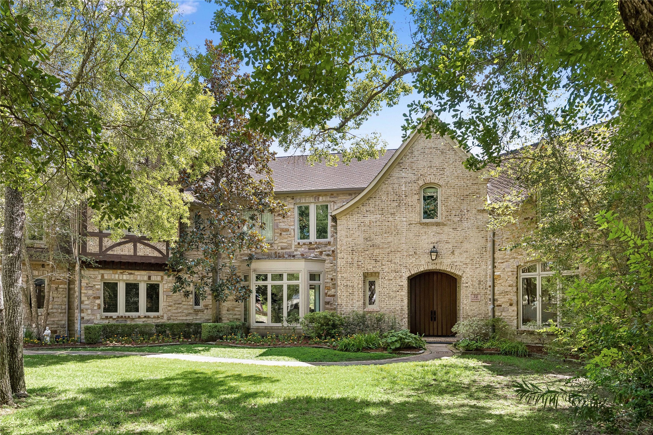 Impressive stone and brick facade featuring timeless architectural details, a welcoming arched entry with double wood doors, and a beautifully landscaped front yard shaded by mature trees. Impressive stone and brick facade featuring timeless architectural details, a welcoming arched entry with double wood doors, and a beautifully landscaped front yard shaded by mature trees.