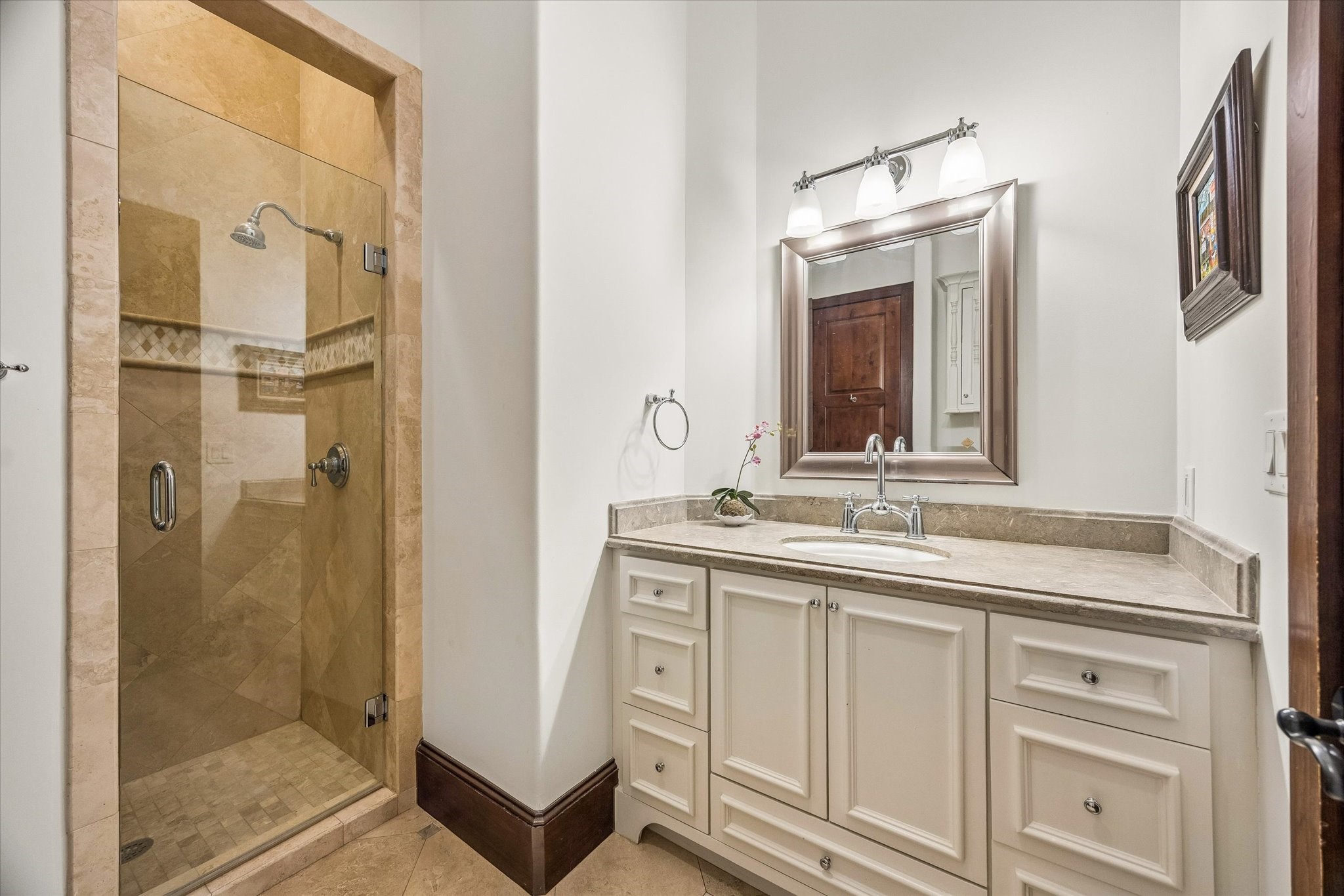 The first-floor guest bath features a stone-topped vanity and a walk-in shower with frameless glass enclosure, natural stone tile, and decorative detailing.