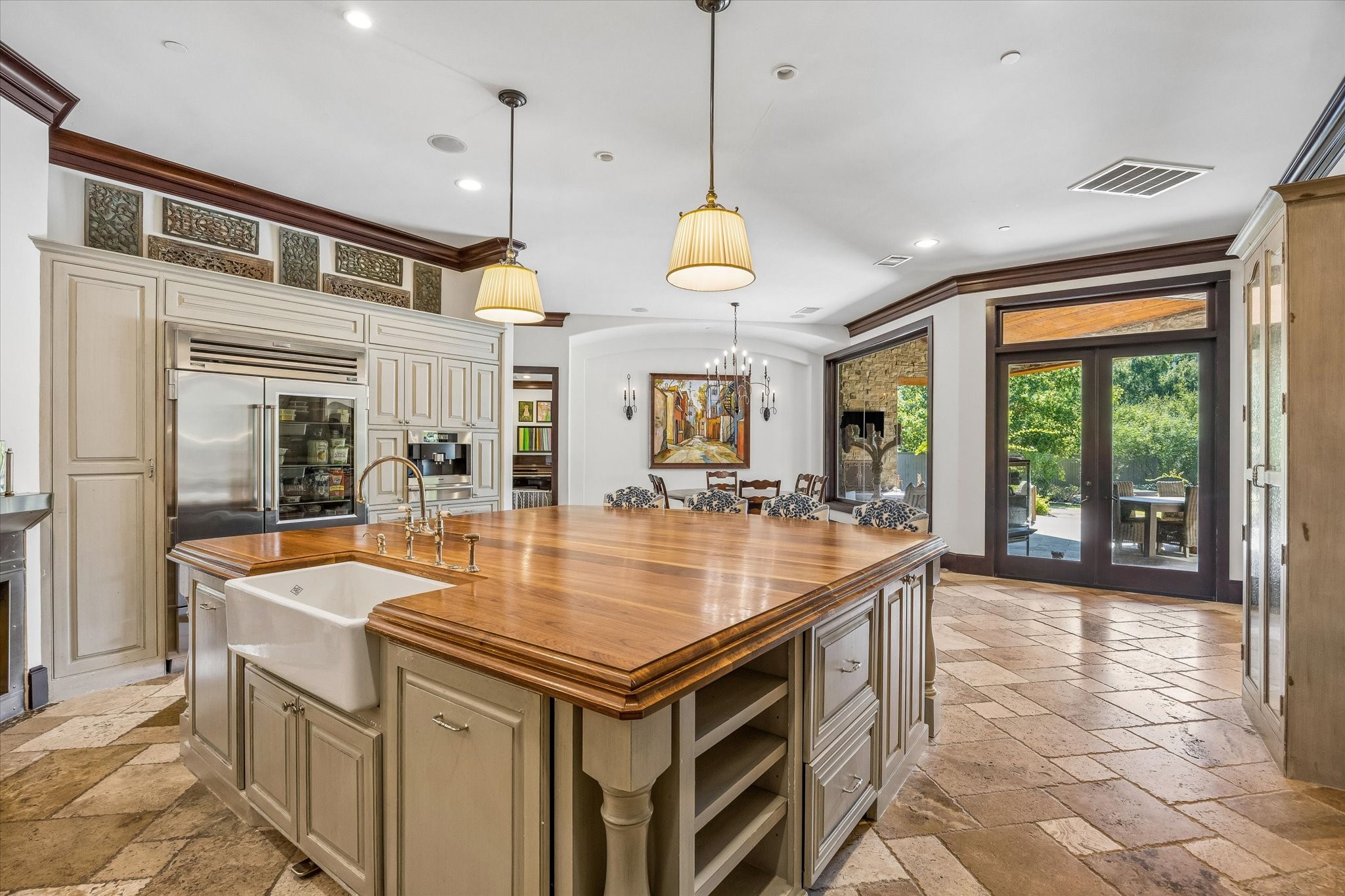 At the heart of the kitchen, a generous wood-topped island with farmhouse sink provides ample workspace, while French doors offer easy access to the covered outdoor living area.