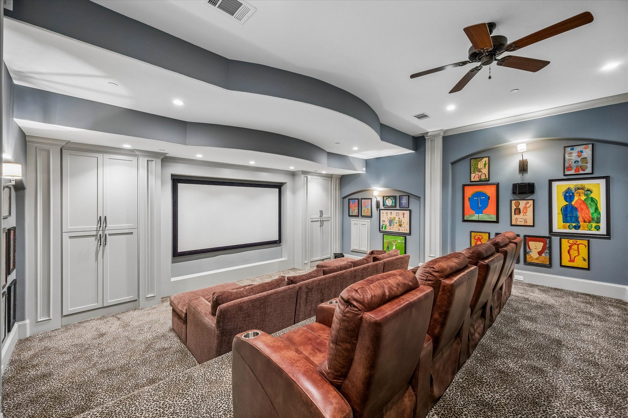 The upstairs media room is designed for movie nights and entertaining, featuring a large projection screen, tiered seating, custom built-ins, and distinctive curved ceiling details.
