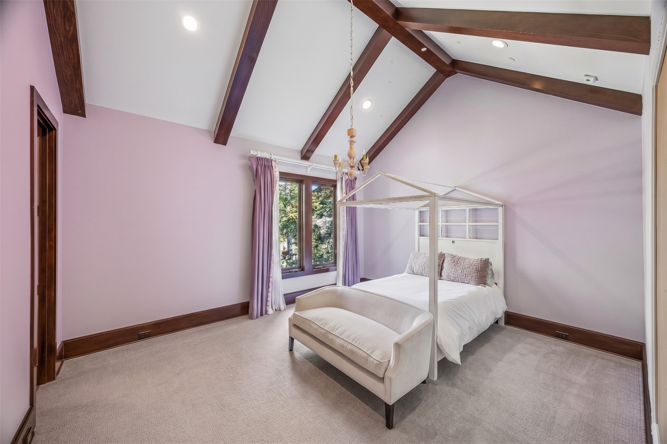 This upstairs bedroom features a vaulted ceiling with exposed wood beams, creating a warm, inviting space with natural light and views of the surrounding trees.