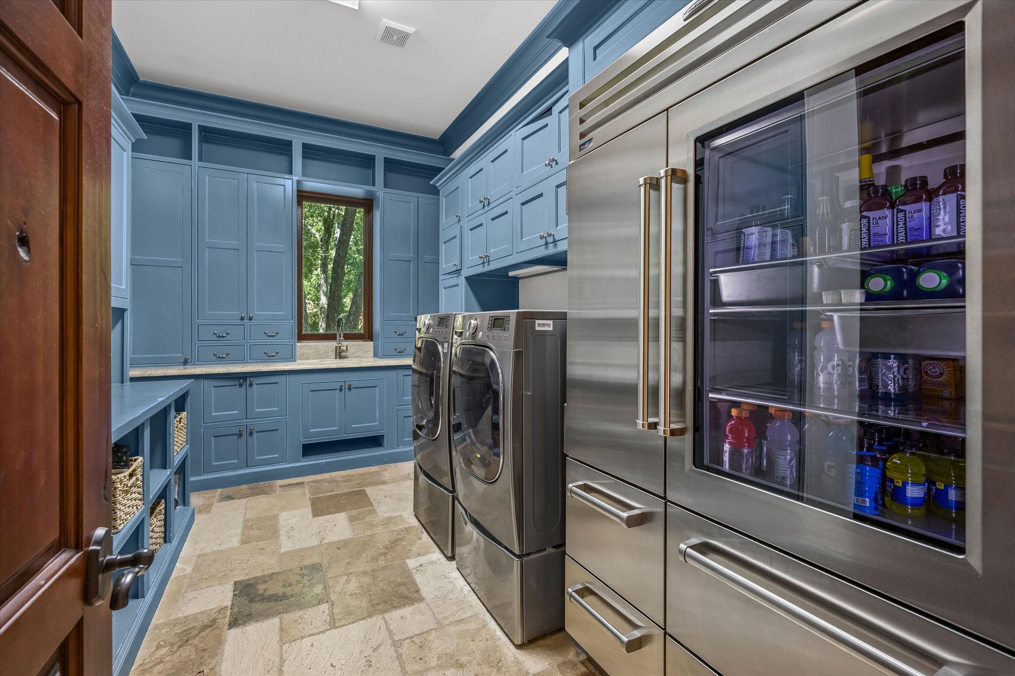 The main utility room combines function and style with custom blue cabinetry, generous storage, a utility sink, space for full-size laundry appliances, and additional refrigeration.