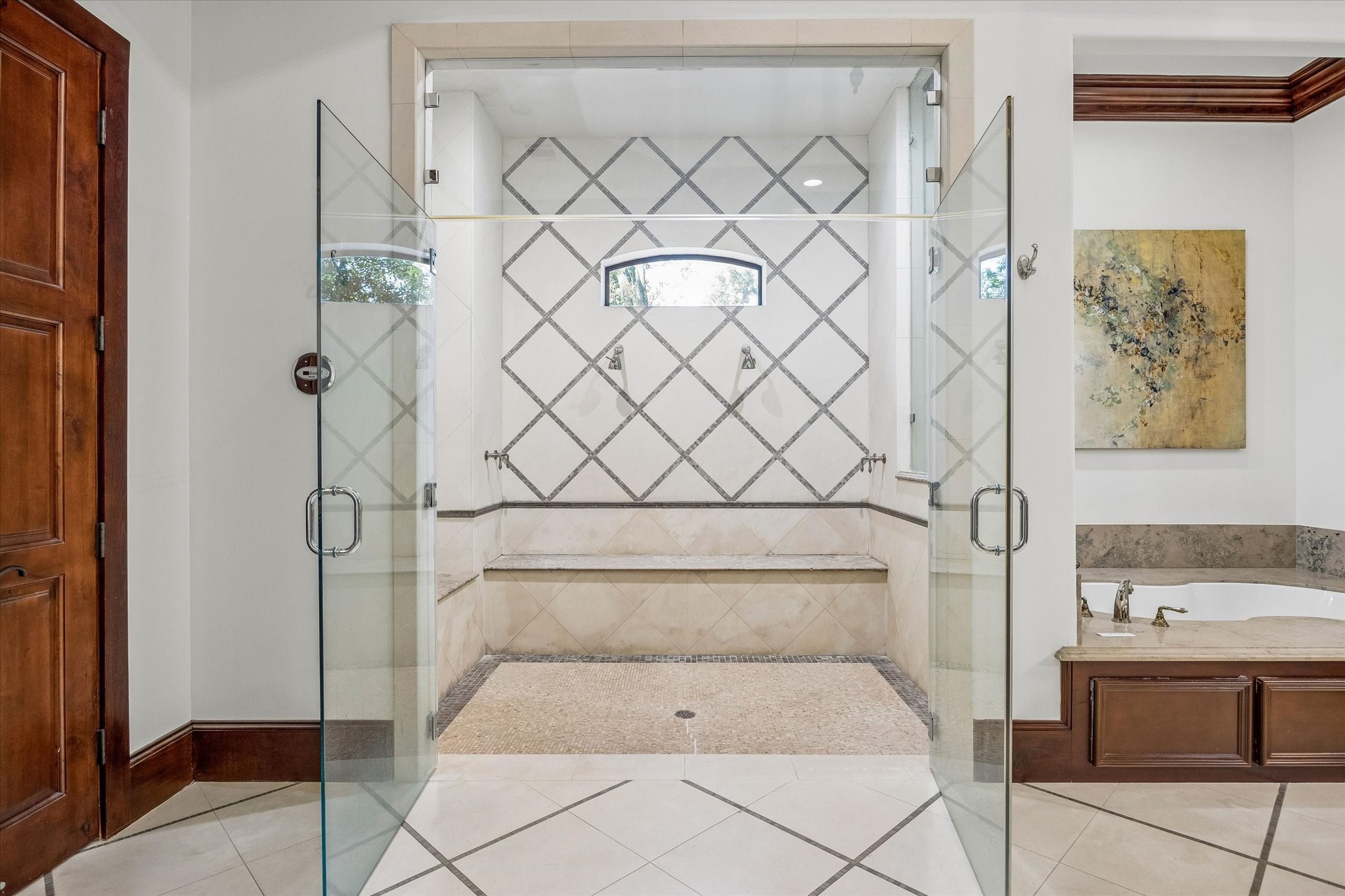 The primary bath features an oversized steam shower with frameless glass doors, dual showerheads, a built-in bench, and decorative tile detailing.