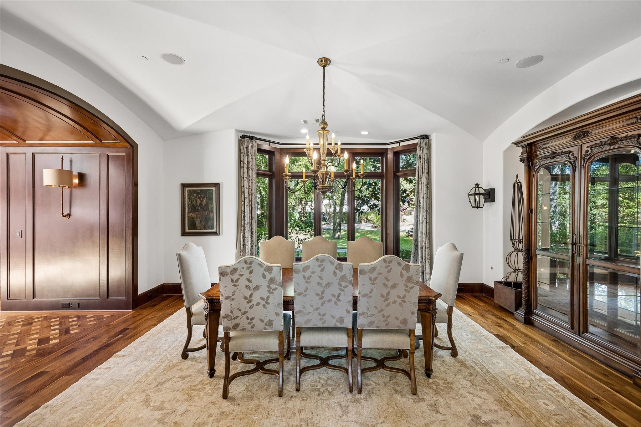 The formal dining room offers a beautiful setting for gatherings, with a graceful vaulted ceiling, rich wood detailing, hardwood floors, and a wall of windows overlooking the front grounds.
