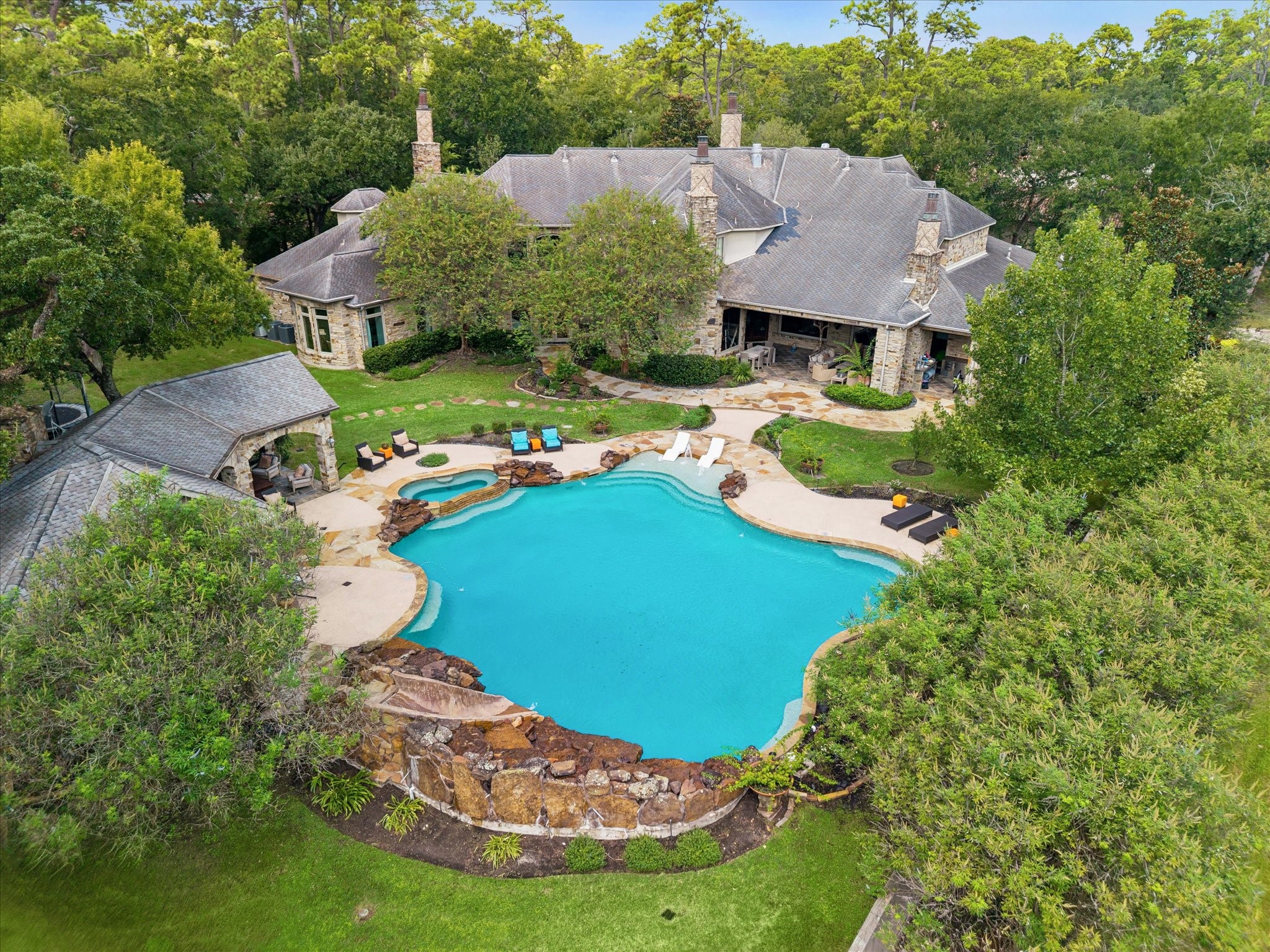 Expansive backyard featuring a resort-style pool with integrated spa, stone waterfalls, generous patio spaces, and multiple covered outdoor living areas ideal for entertaining.