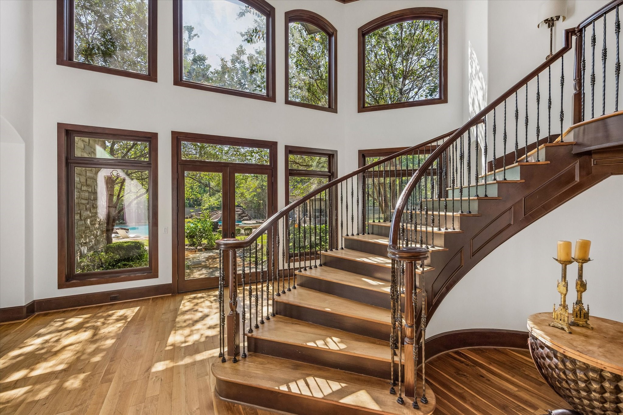 The sweeping staircase leads upstairs, framed by soaring two-story windows that fill the entry with natural light and offer beautiful views of the backyard and pool.