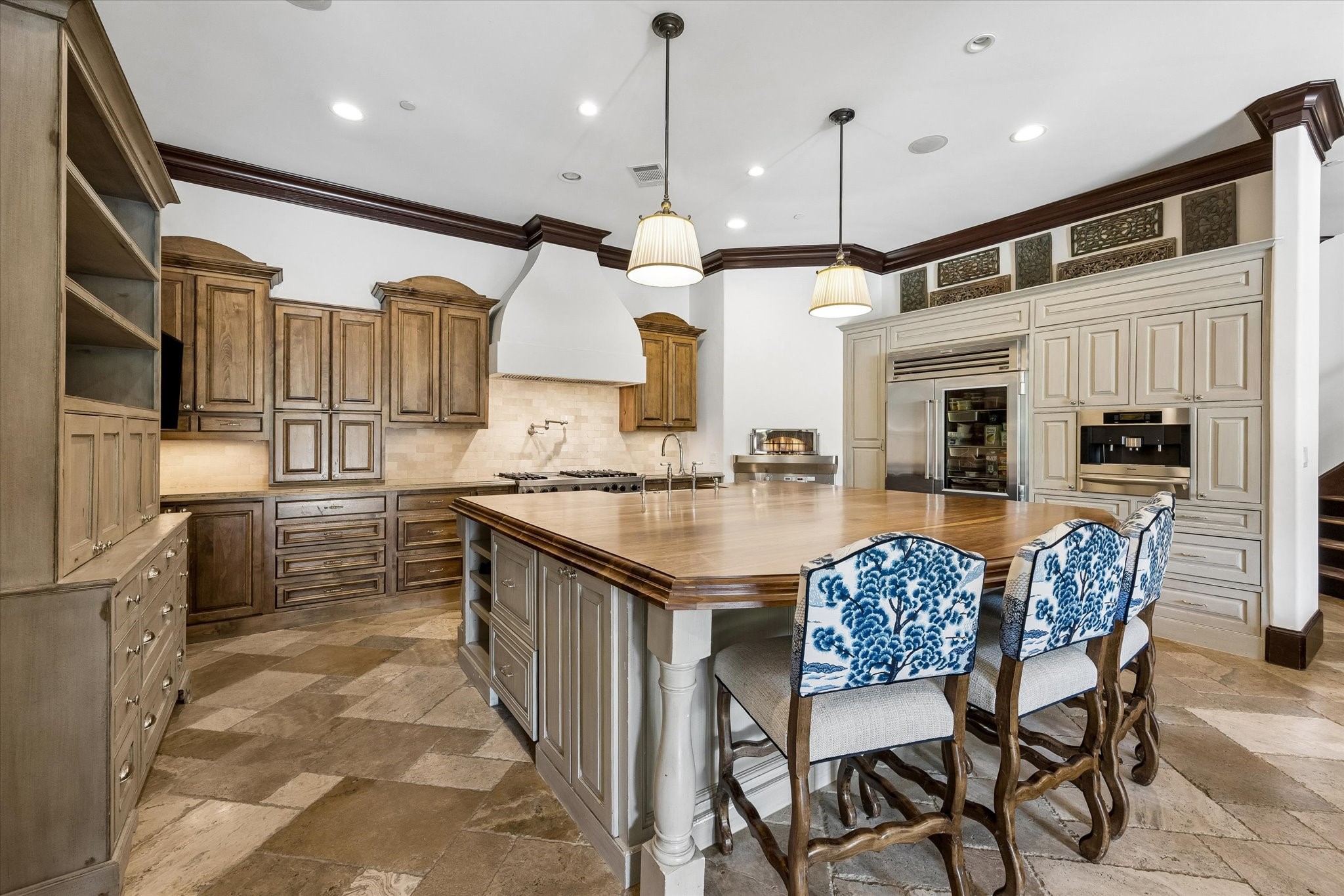 A different perspective of the kitchen showcases the generous proportions, contrasting cabinetry, natural stone flooring, and decorative architectural details that give the space its distinctive character.