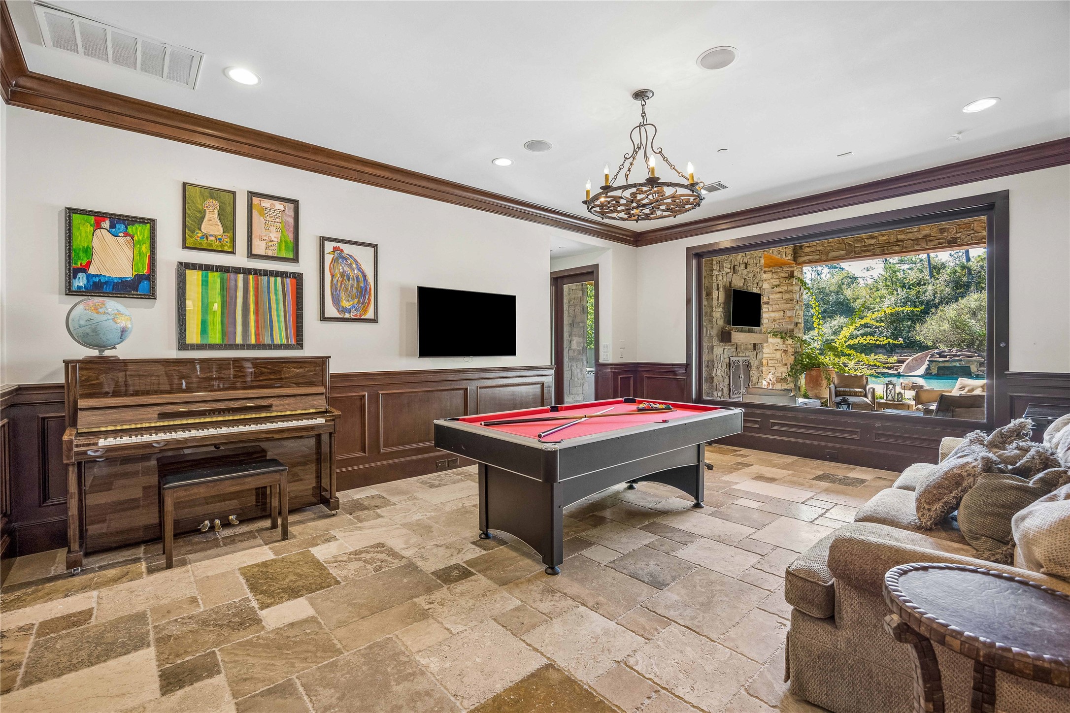 The downstairs game room offers a spacious setting for recreation and entertaining, with stone flooring, rich wood wainscoting, and a large picture window overlooking the covered patio and pool.