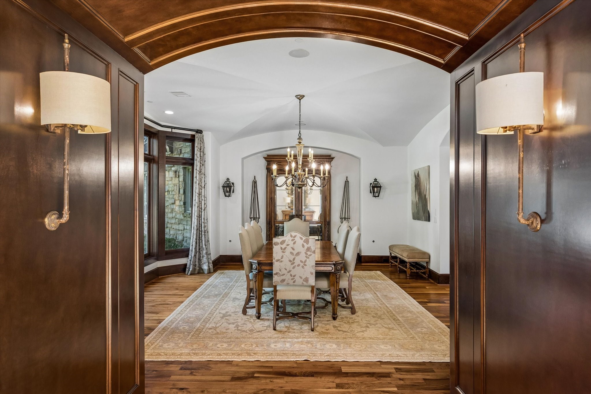 An elegant transition into the formal dining room, where rich wood paneling and an arched entry open to a spacious room with a graceful barrel-vaulted ceiling, hardwood floors, and natural light.