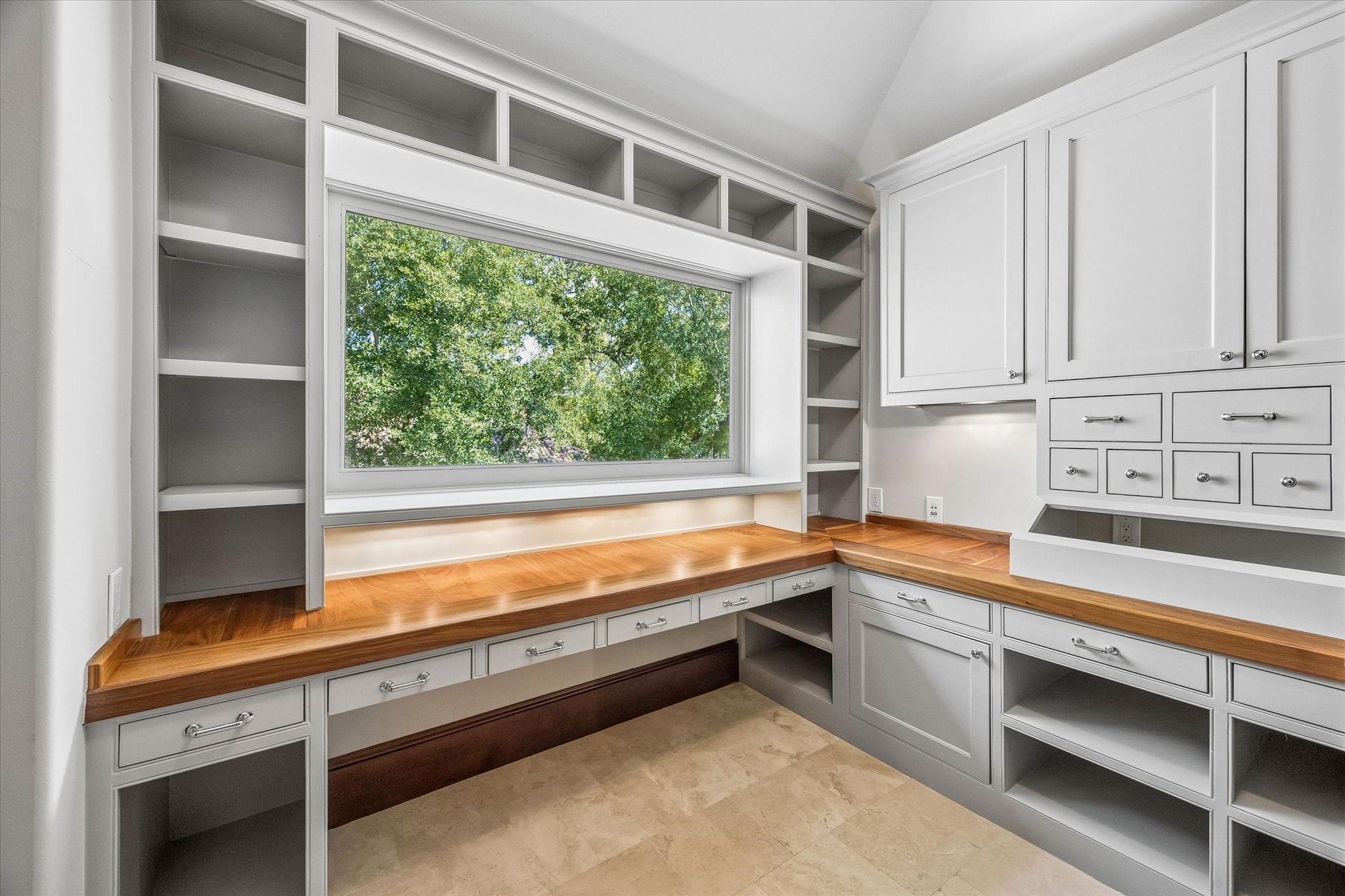 A thoughtfully designed craft room offers abundant built-in storage, generous work surfaces, and a large window that brings natural light into the space.
