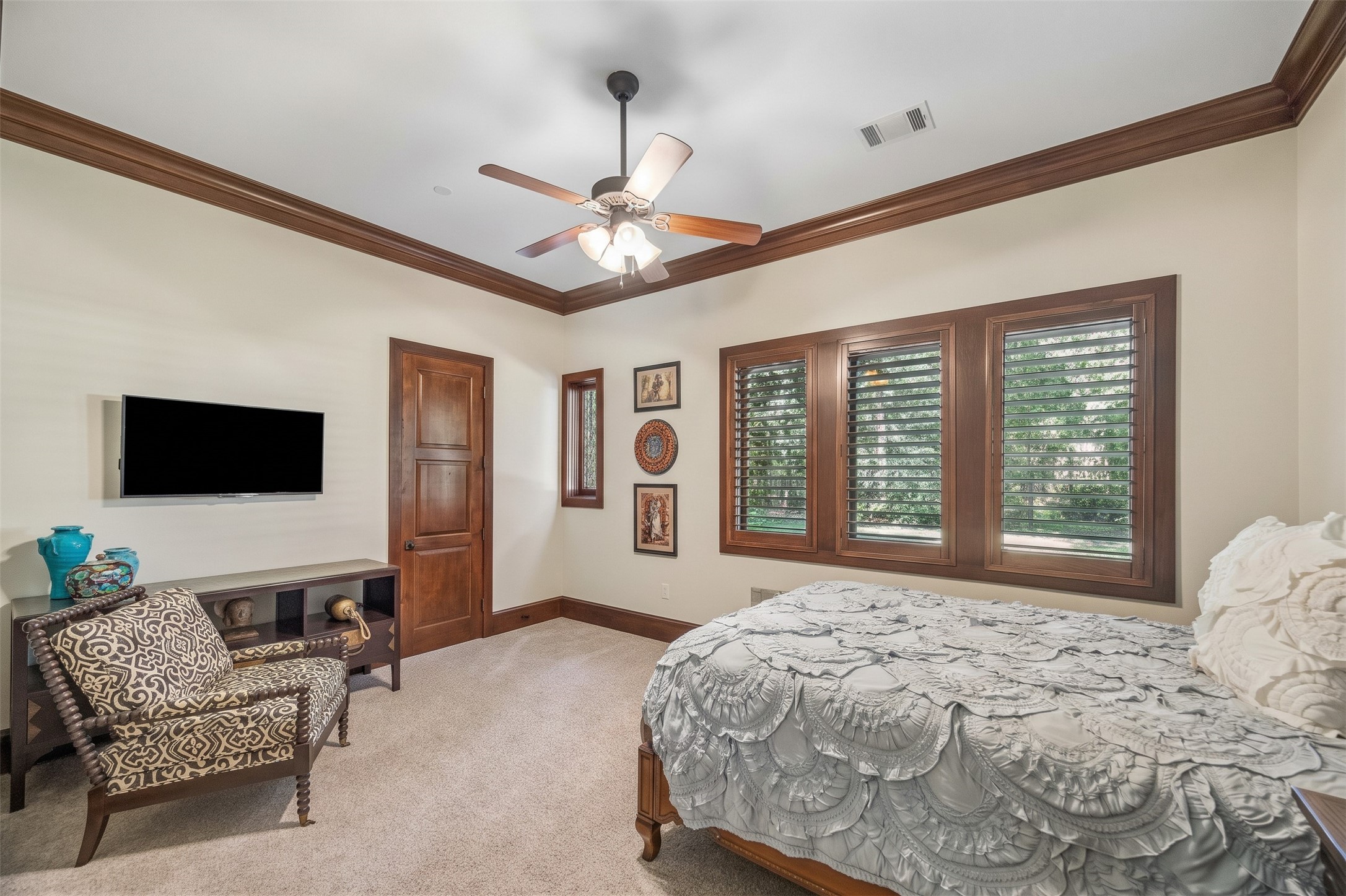 The first-floor guest bedroom offers a comfortable retreat with generous proportions, soft carpeting, and windows with plantation shutters overlooking the grounds.