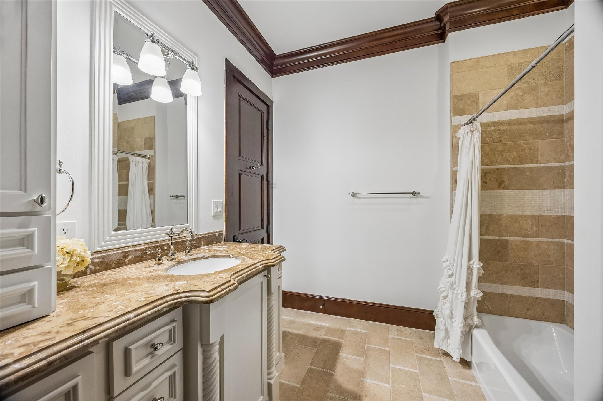 The adjoining bath features a stone-topped vanity with custom cabinetry, natural stone flooring, and a tub and shower combination with decorative tile accents.