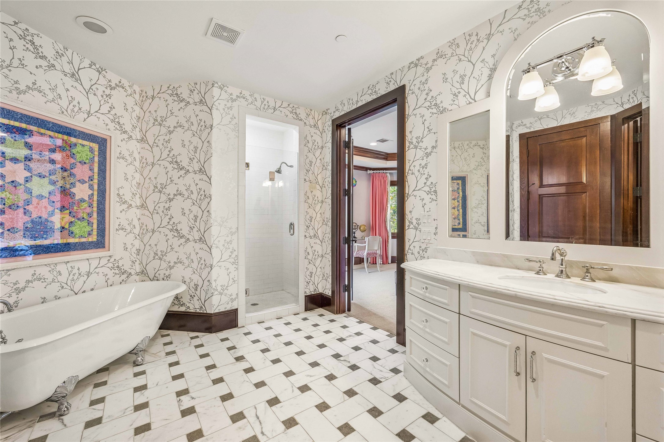 The adjoining bath features a classic clawfoot soaking tub, separate walk-in shower, marble-patterned tile flooring, and delicate botanical wallcovering.