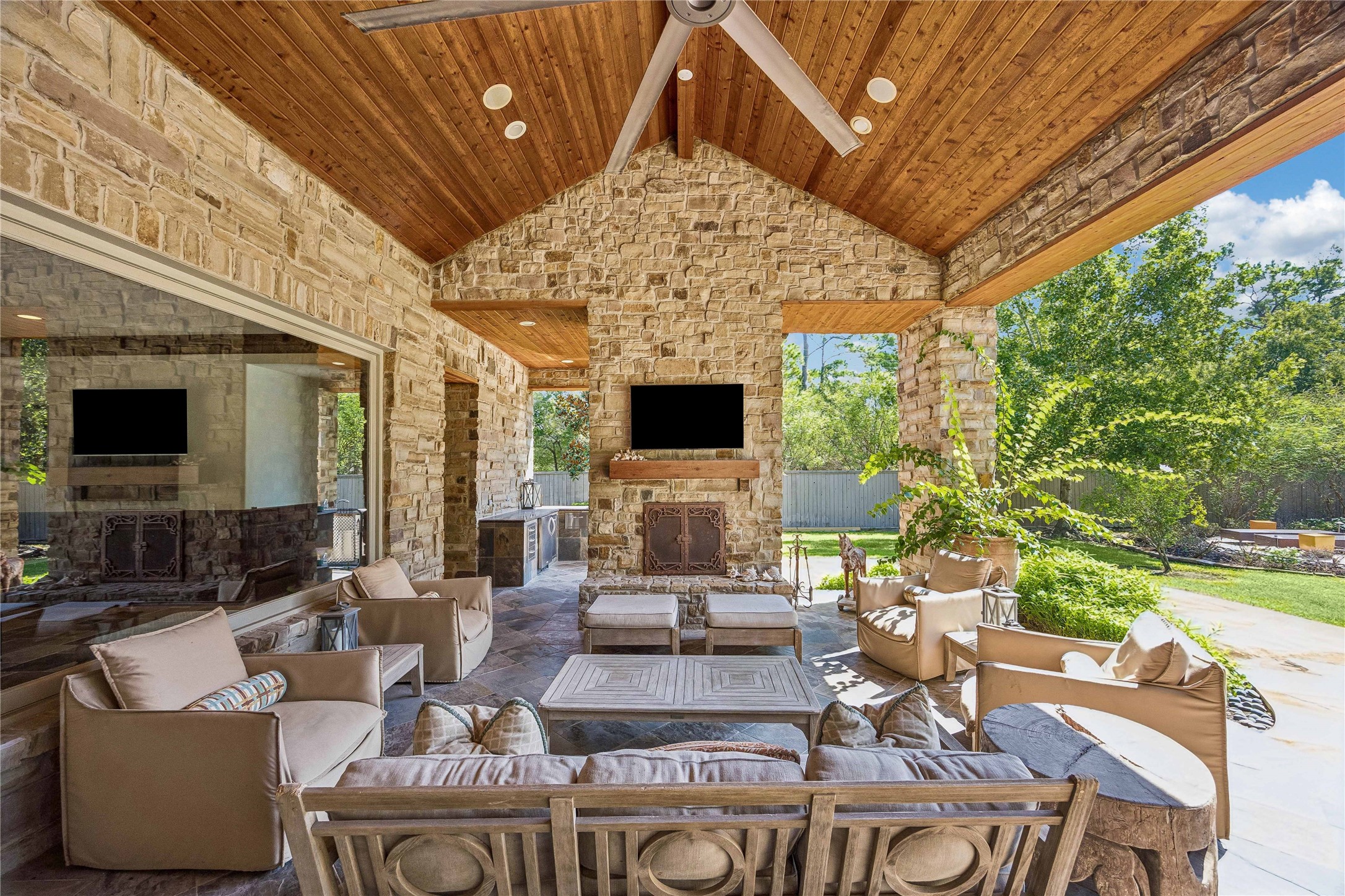 Designed for year-round entertaining, the expansive covered patio offers a seamless transition between indoor and outdoor living, with a soaring wood-plank ceiling, stone fireplace, and views of the resort-style pool.