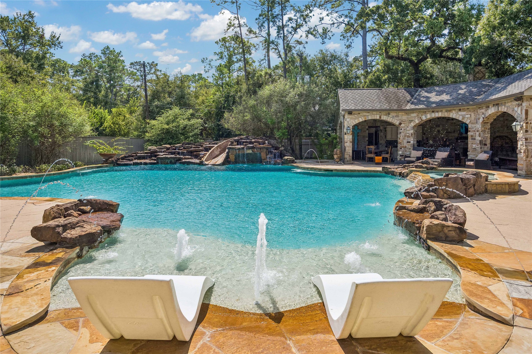 The pool's custom design includes a stone waterfall, waterslide, and multiple water features, with a covered outdoor pavilion just steps away.