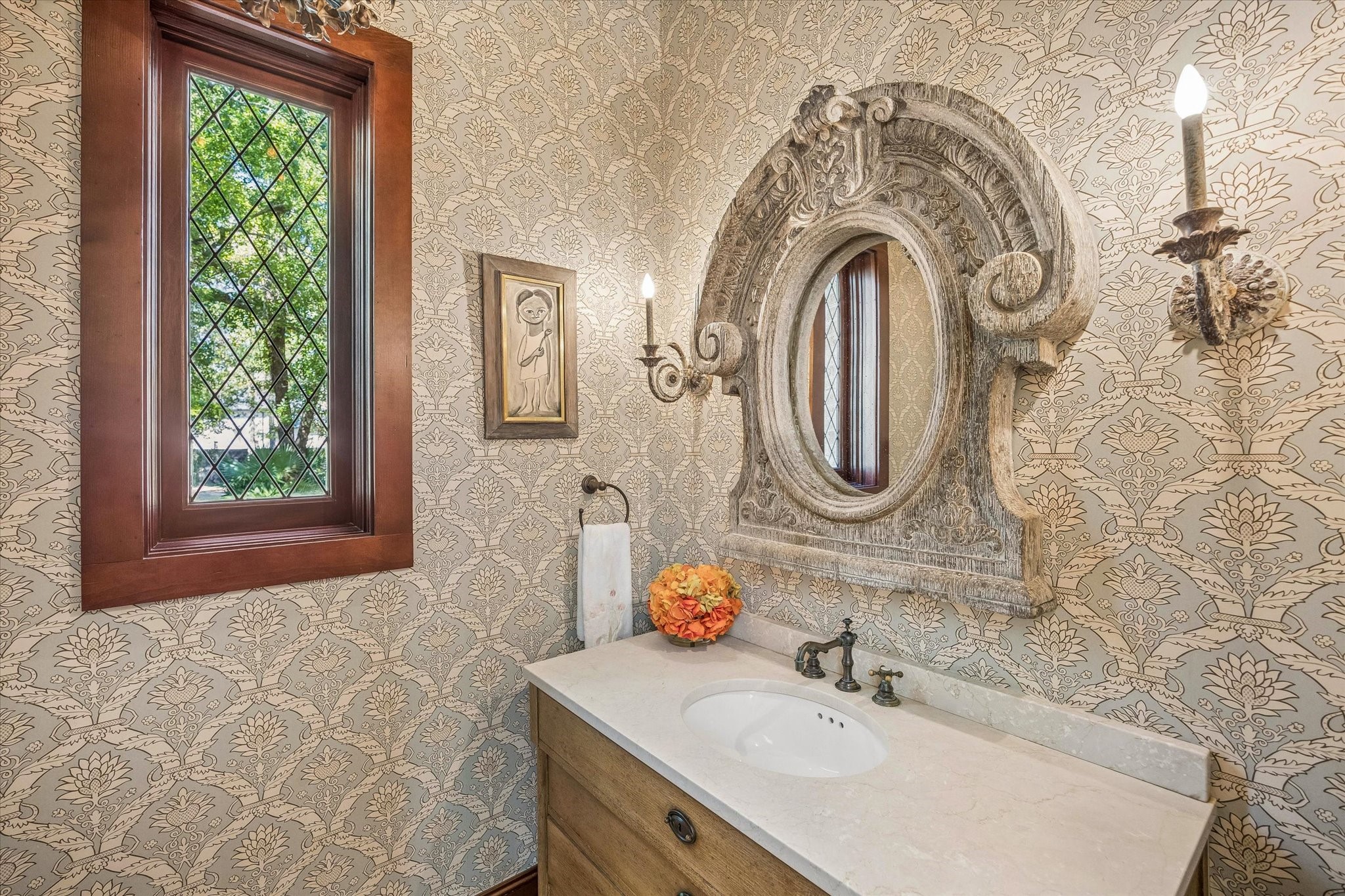 The formal powder room features elegant patterned wallcovering, a stone-topped vanity, leaded glass window, and traditional architectural details.
