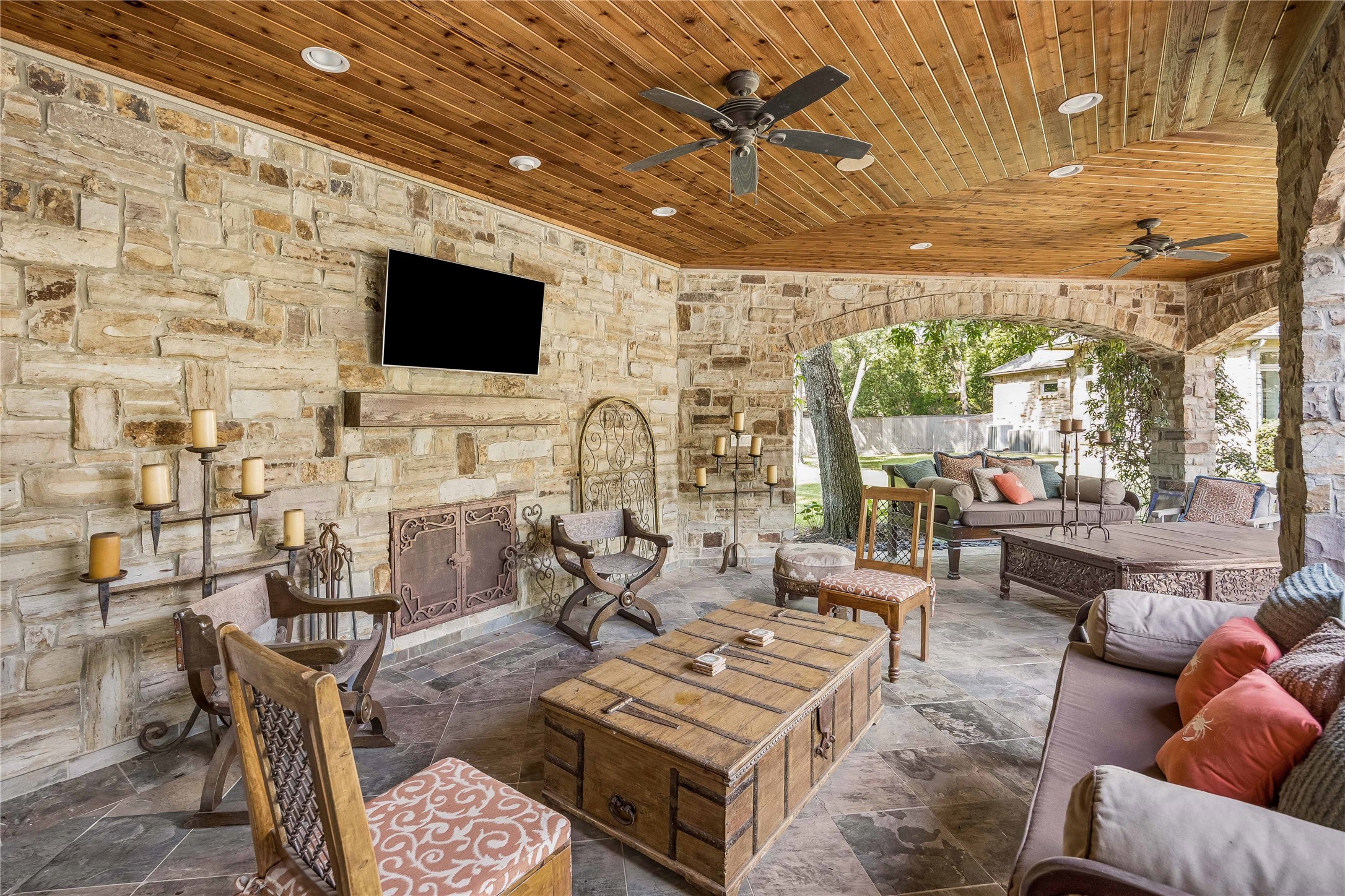 A separate stone pavilion offers an inviting outdoor retreat with a beautiful fireplace, natural stone flooring, and a warm wood-plank ceiling.