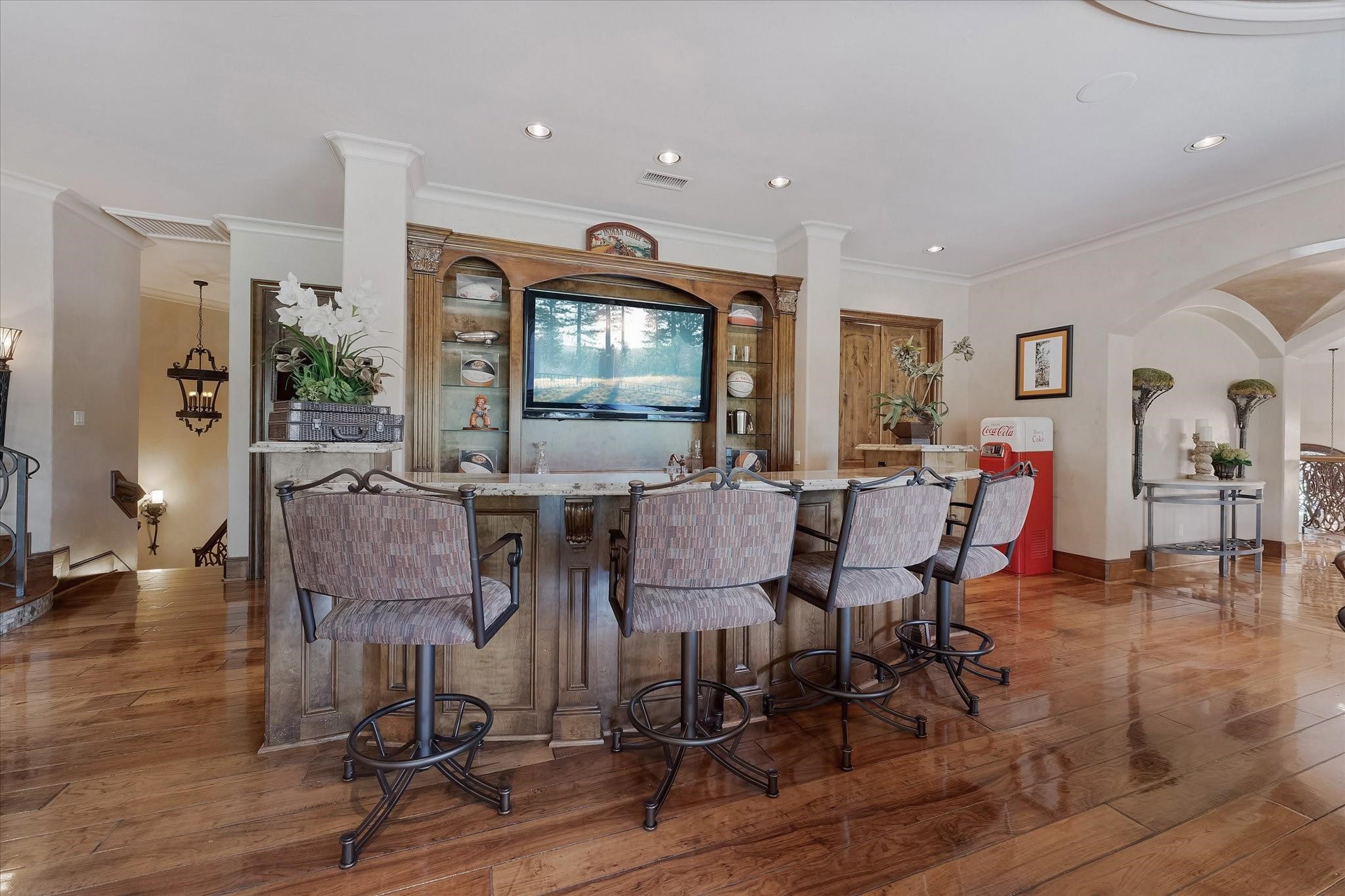 Full galley-style Bar with sink, Ice Machine, and Sub-Zero Beverage Chiller. two-level granite countertops with countertop seating, built-in shelves with millwork, Lower cabinets, and Drawers Providing Ample Storage behind the bar. Adjacent to the bar is a large Storage room/Wrapping room.