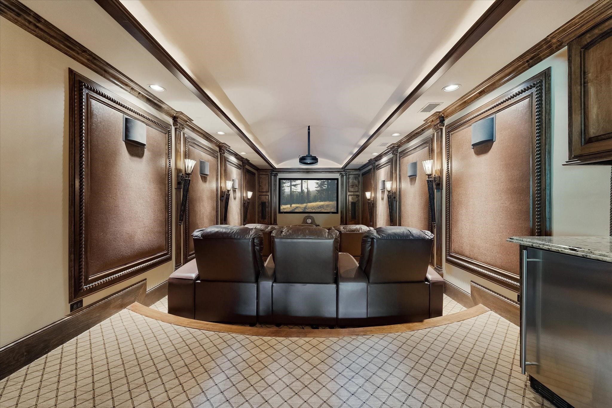 The theater room, located above the garage with sound deadening decorative panels. features nine electrical adjustable seats arranged in a stadium seating configuration. Built-in beverage cooler & Microwave, built-in projector screen, projector, and surround sound system. Custom millwork & crown molding, Designer carpet flooring with hardwood leading edges along with barrel ceiling controlled recessed & tray cove lighting, & sconce torch lighting enhances the ambiance.