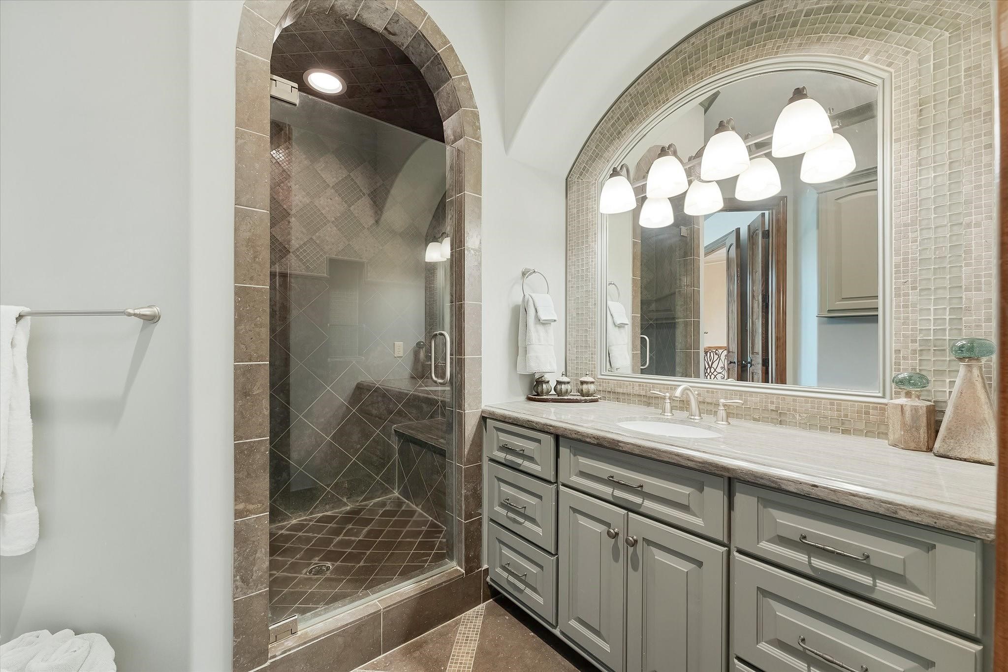 Guest bedroom ensuite #2 on the second floor.
Dual Adler wood doors lead to the Ensuite with custom tile flooring with an intricate pattern and a shower with a built-in bench. Granite countertop vanity with Custom framed mirror. Walk-in Closet With Built-ins and Door Jamb Light Switch.