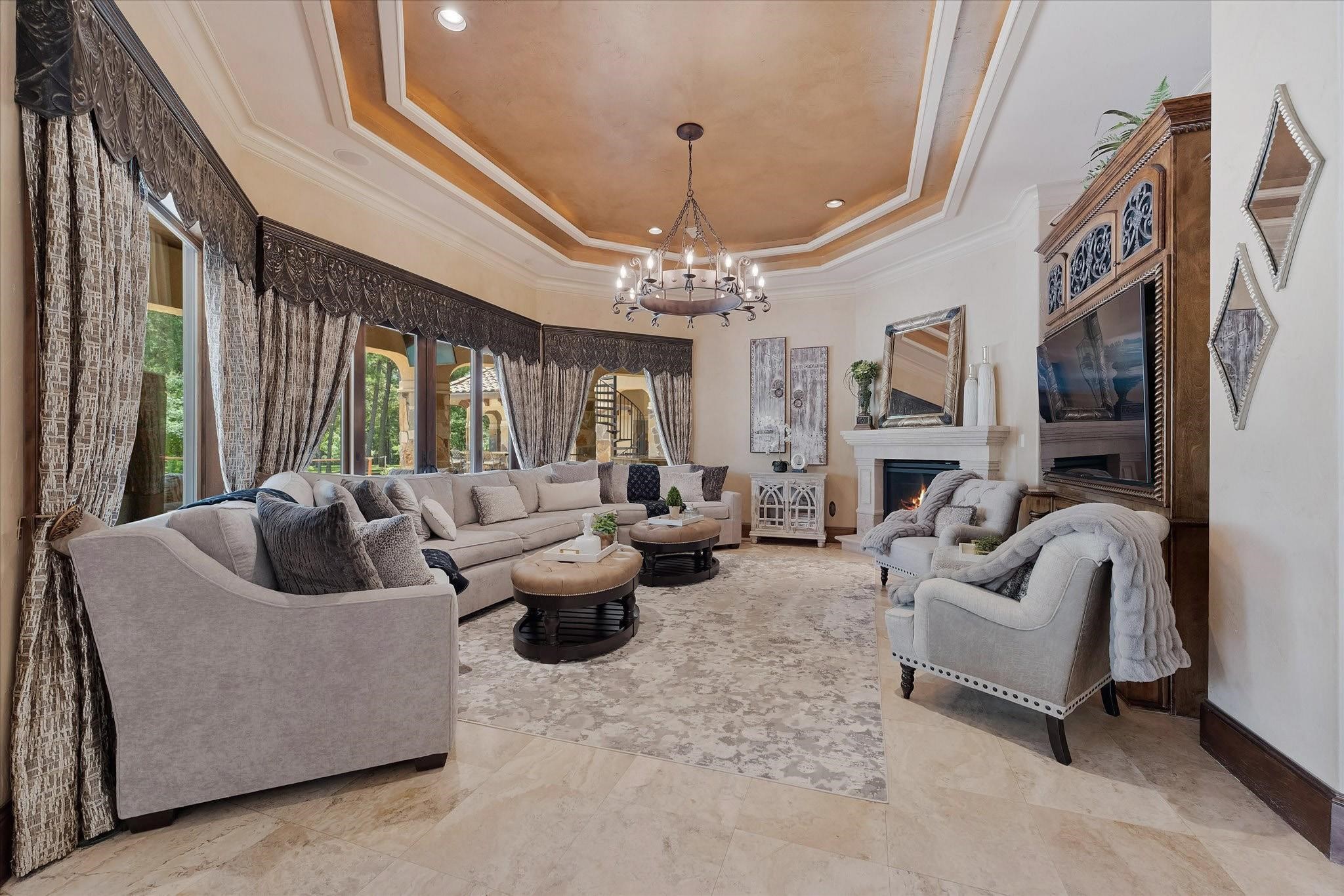 Great Room with fireplace, built-in entertainment center featuring extensive millwork, large bay windows, and sliding doors. Tray ceiling with cove lighting and crown molding, recessed lighting, and surround sound speakers.