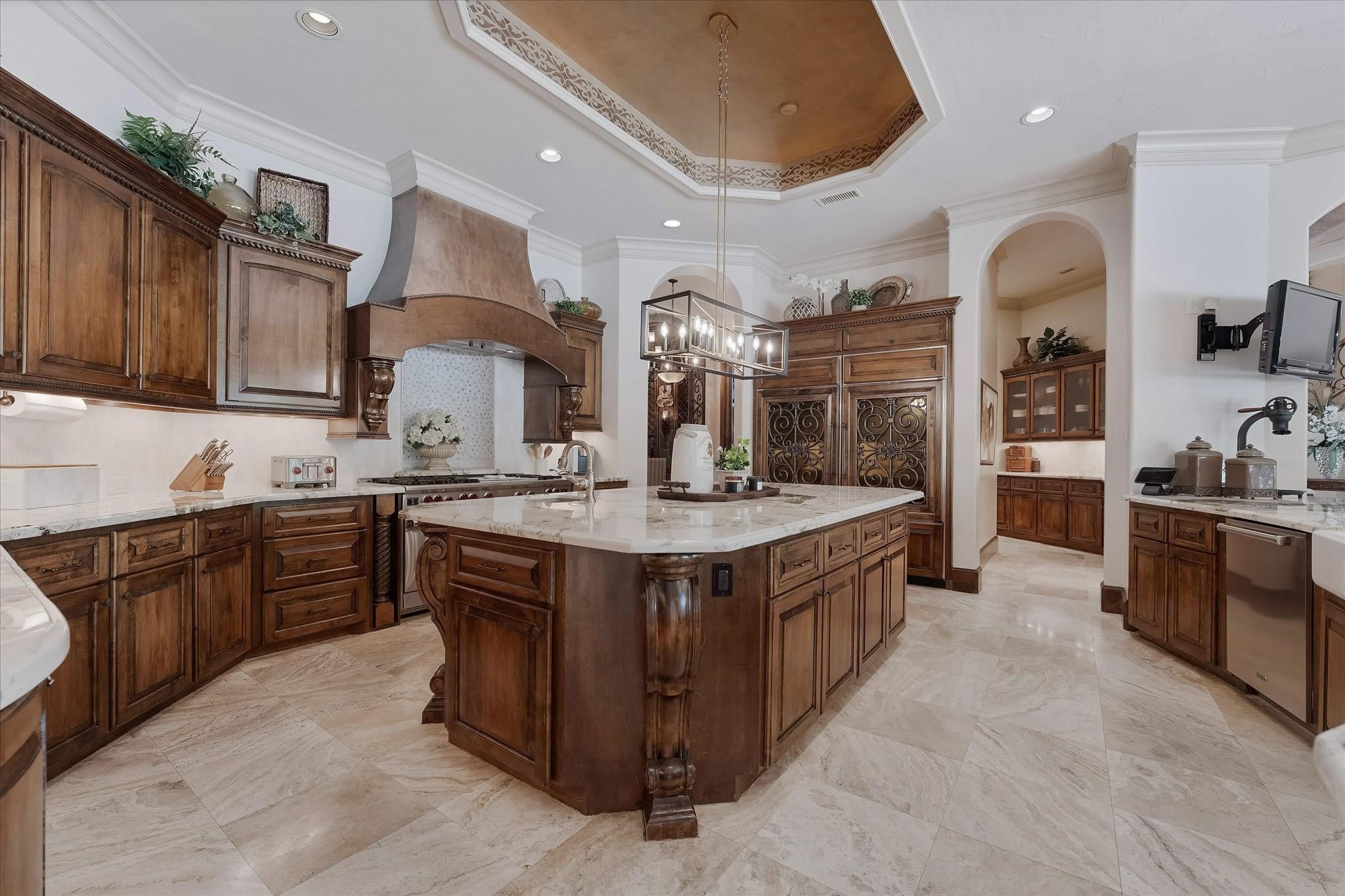 The kitchen boasts a 60" gas range with double ovens, warming drawer, two full-sized stainless dishwashers, a stainless steel ice maker, and dual Sub-Zero refrigerators with freezer drawers. The oversized walk-in pantry features a full-size SubZero refrigerator. Alpine granite countertops, an oversized center island, recessed speakers and lighting, pendant light fixtures, custom crown molding, travertine floors, a tray ceiling with cove lighting, and under-cabinet lighting.