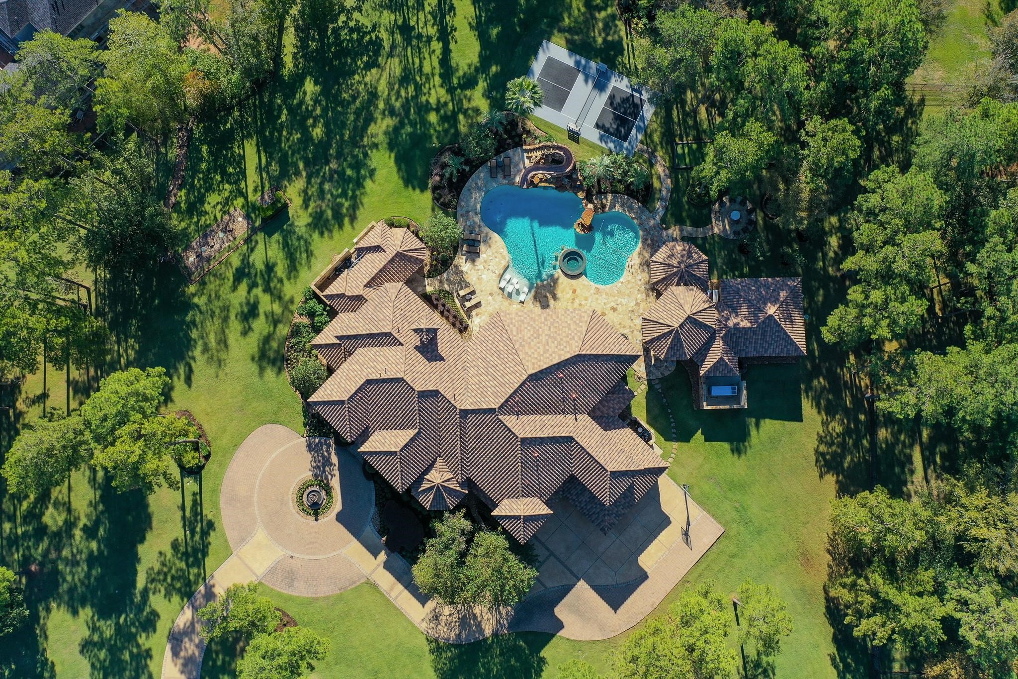 The expansive outdoor entertainment area includes a pickleball court, resort-style pool, bocce ball Court, wood burning fire pit with seating area surrounding it ,Summer Kitchen With Granite Countertop, Gas Grill With Side Burner, Sink, and outdoor fridge., entertainment pavilion with a fireplace and seating area that connects to the guest house, glass fire pit table, and a full outdoor bath.