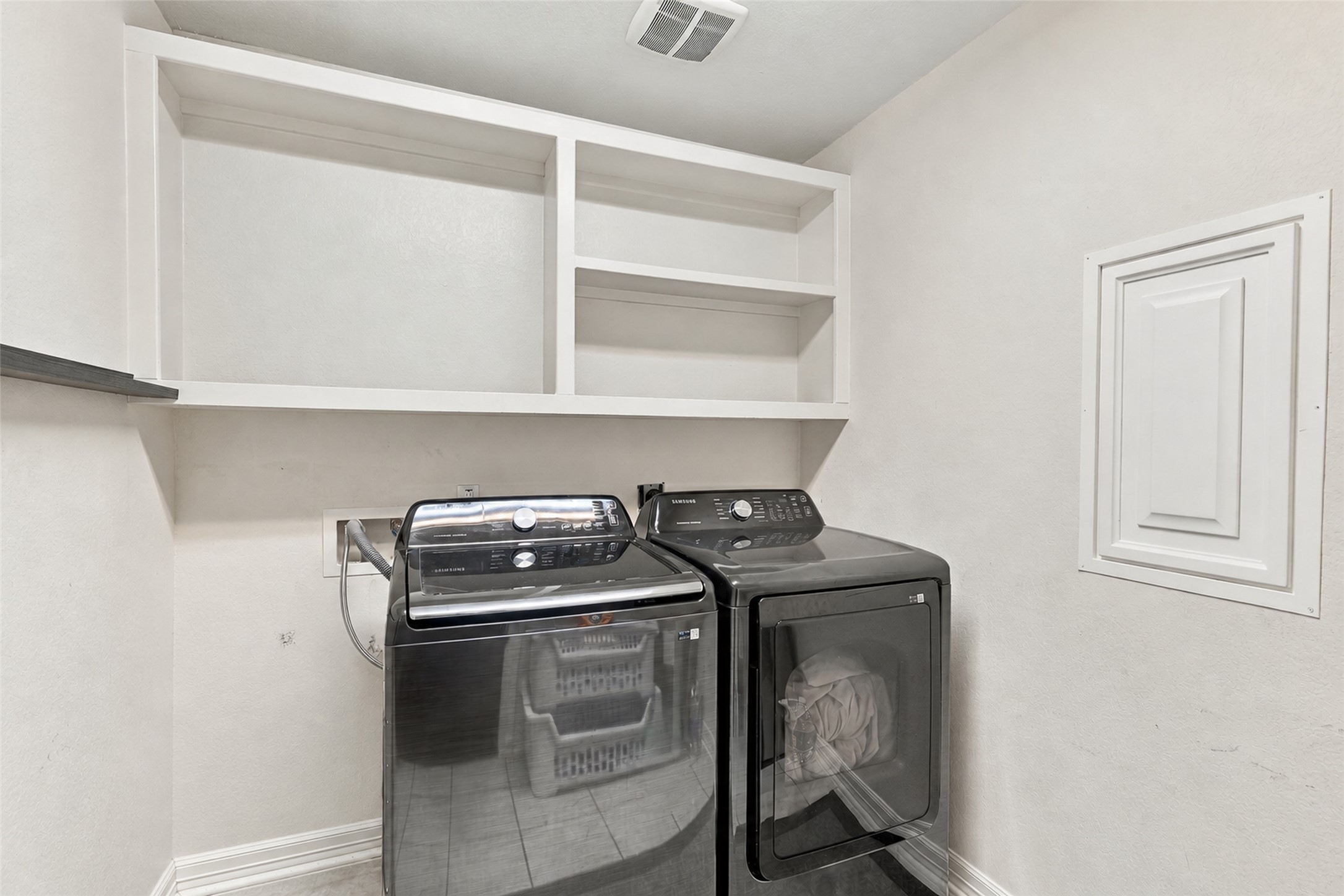 Laundry room with washer and dryer, overhead shelving, and additional storage space.