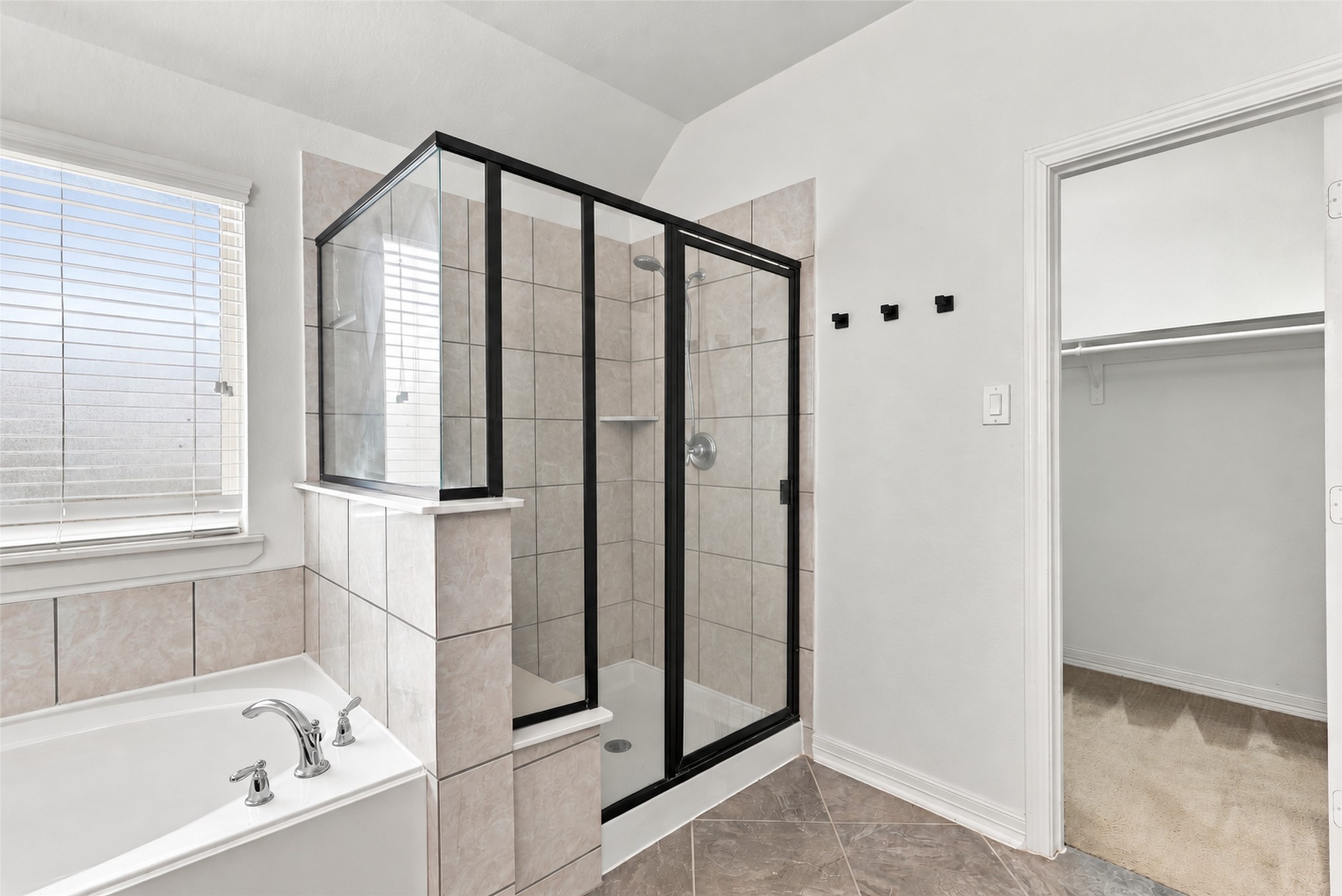 Additional primary bathroom view featuring the glass-enclosed shower, soaking tub, and walk-in closet access.