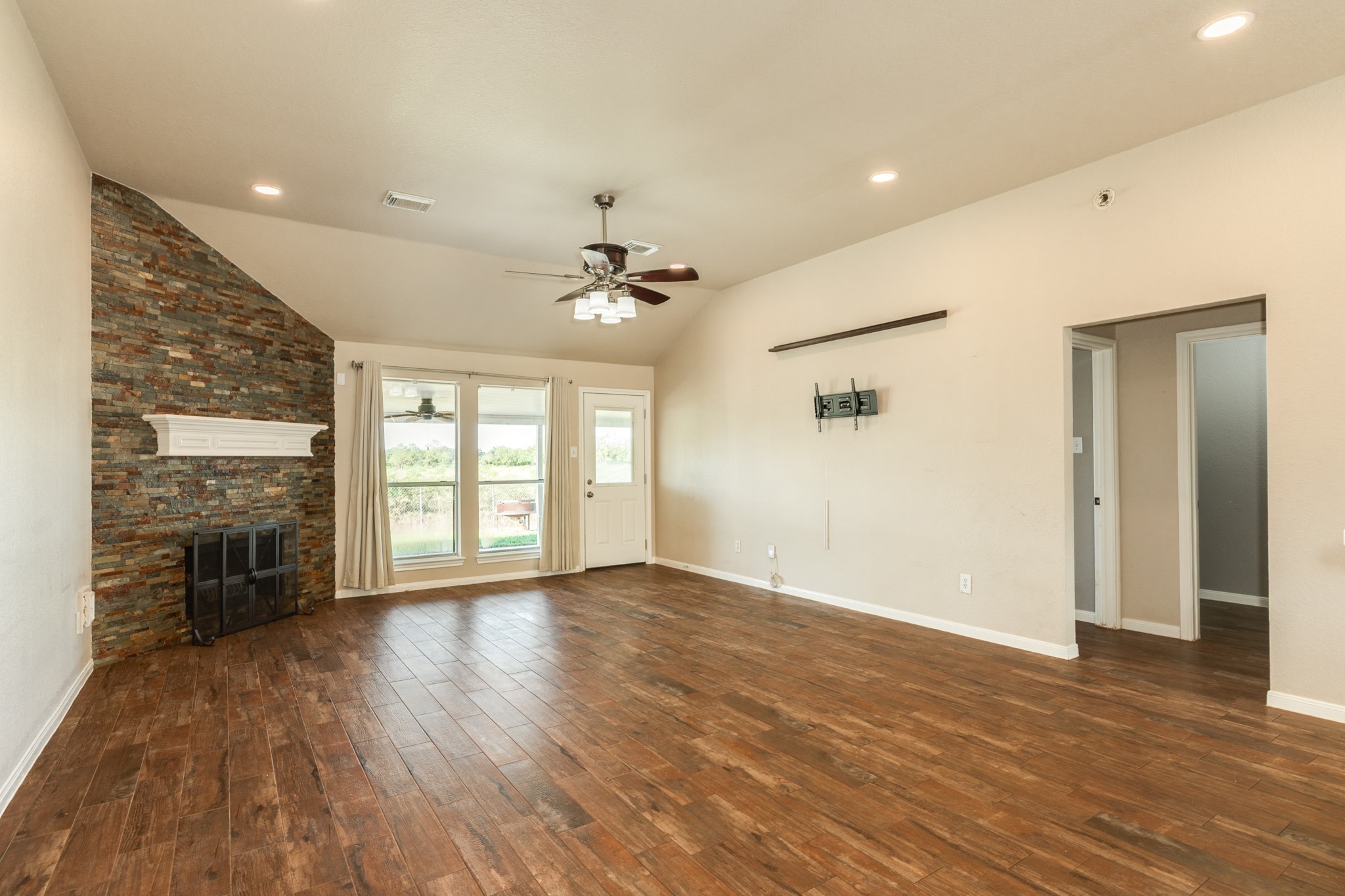 Spacious living room with beautiful wood look tile flooring, a striking corner fireplace, and abundant natural light from large windows.