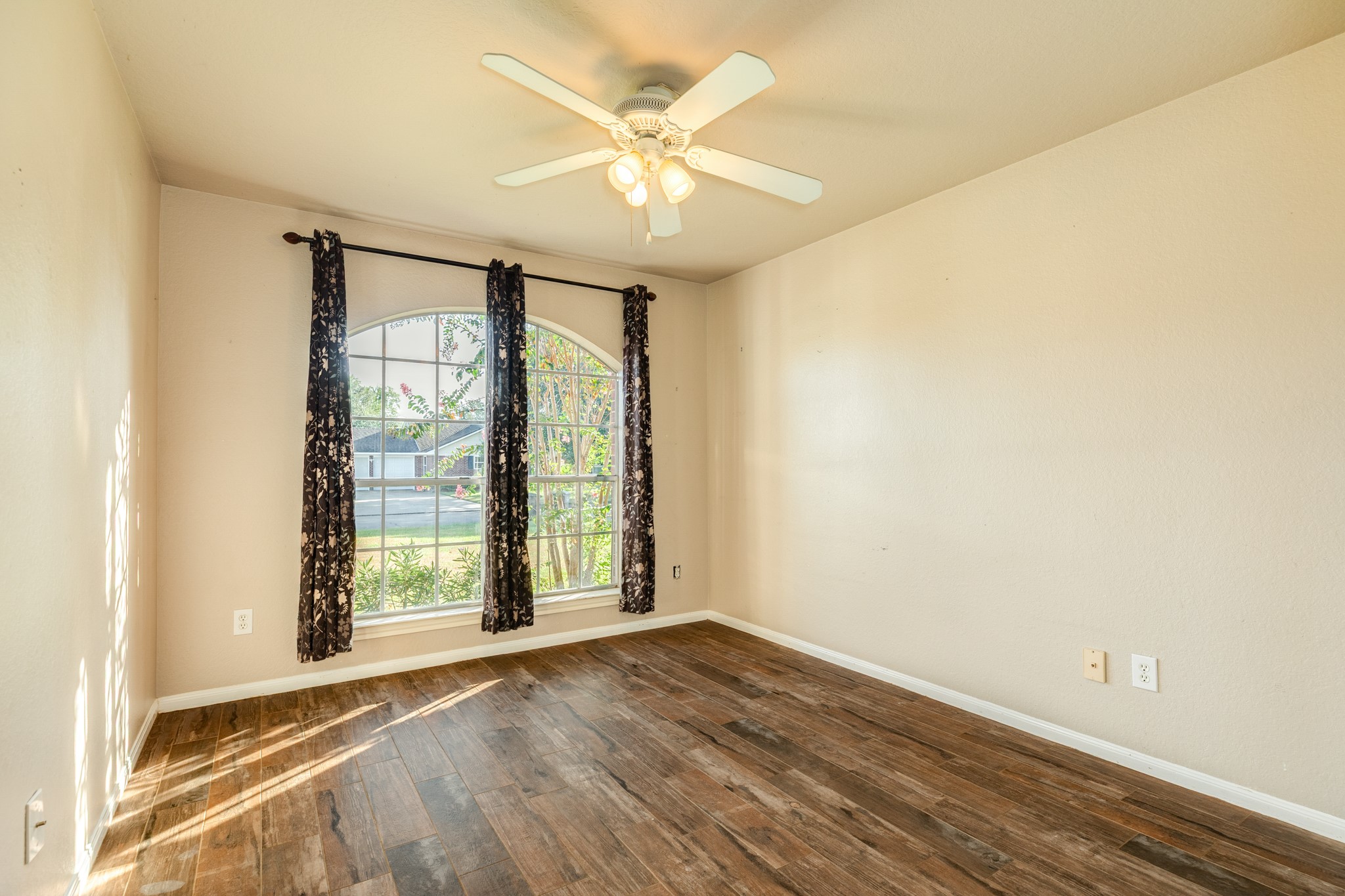 Secondary bedroom with a large arched window plus a ceiling fan for comfort.