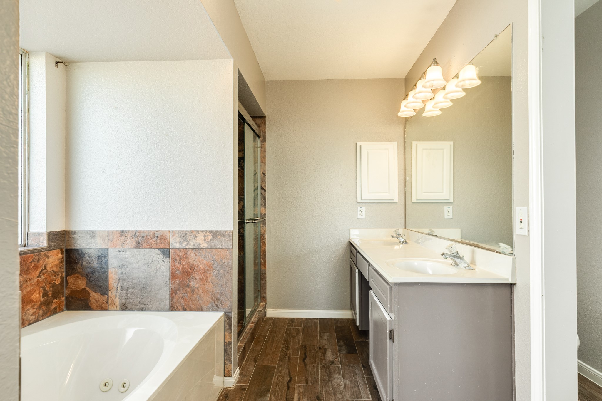 Spacious primary bathroom featuring a luxurious jetted tub, dual sinks, sleek tile flooring, and a large mirror with elegant lighting.