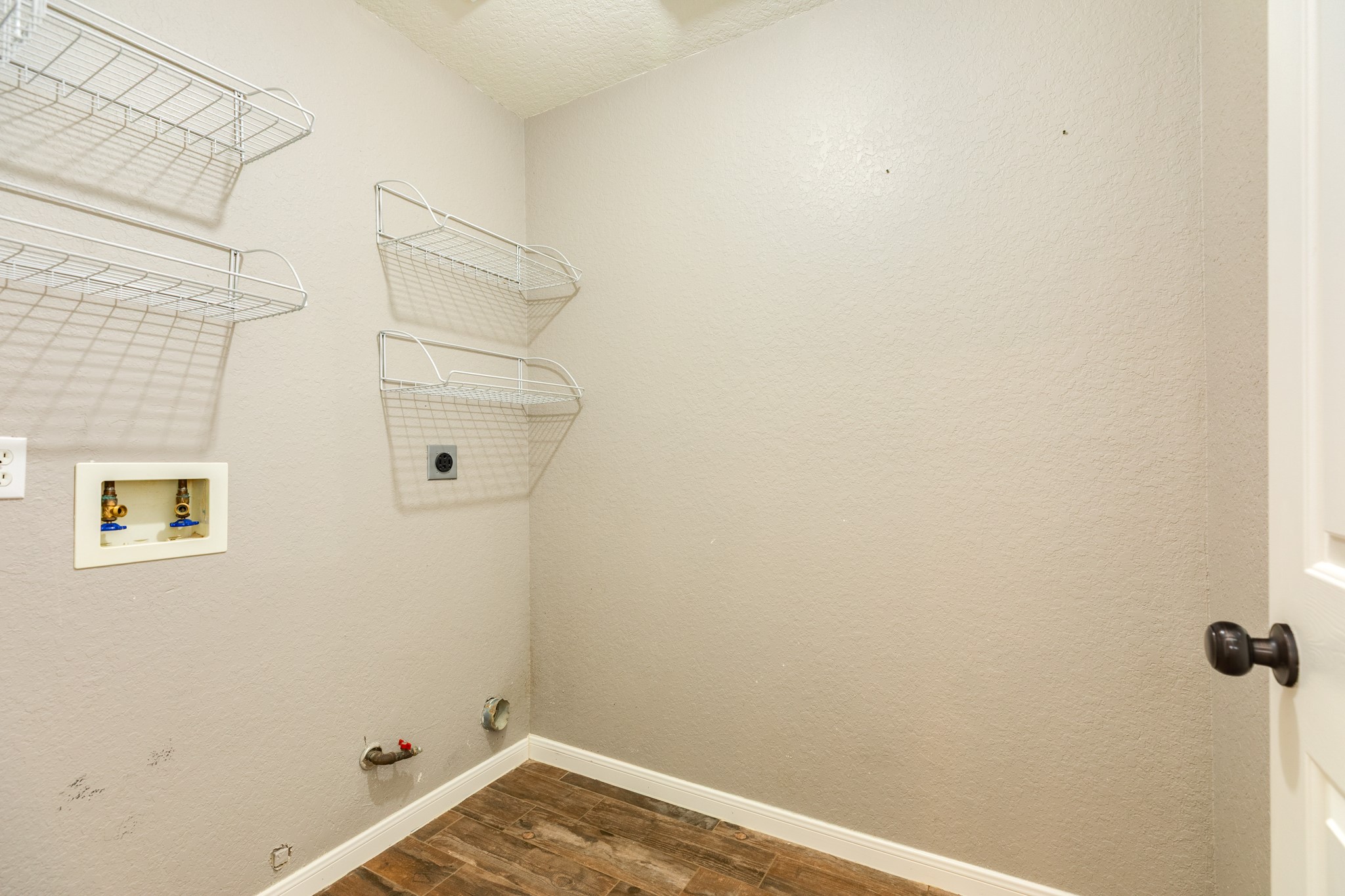 Spacious laundry room with wall-mounted wire shelving, washer and dryer hookups, and durable flooring for convenience and functionality.