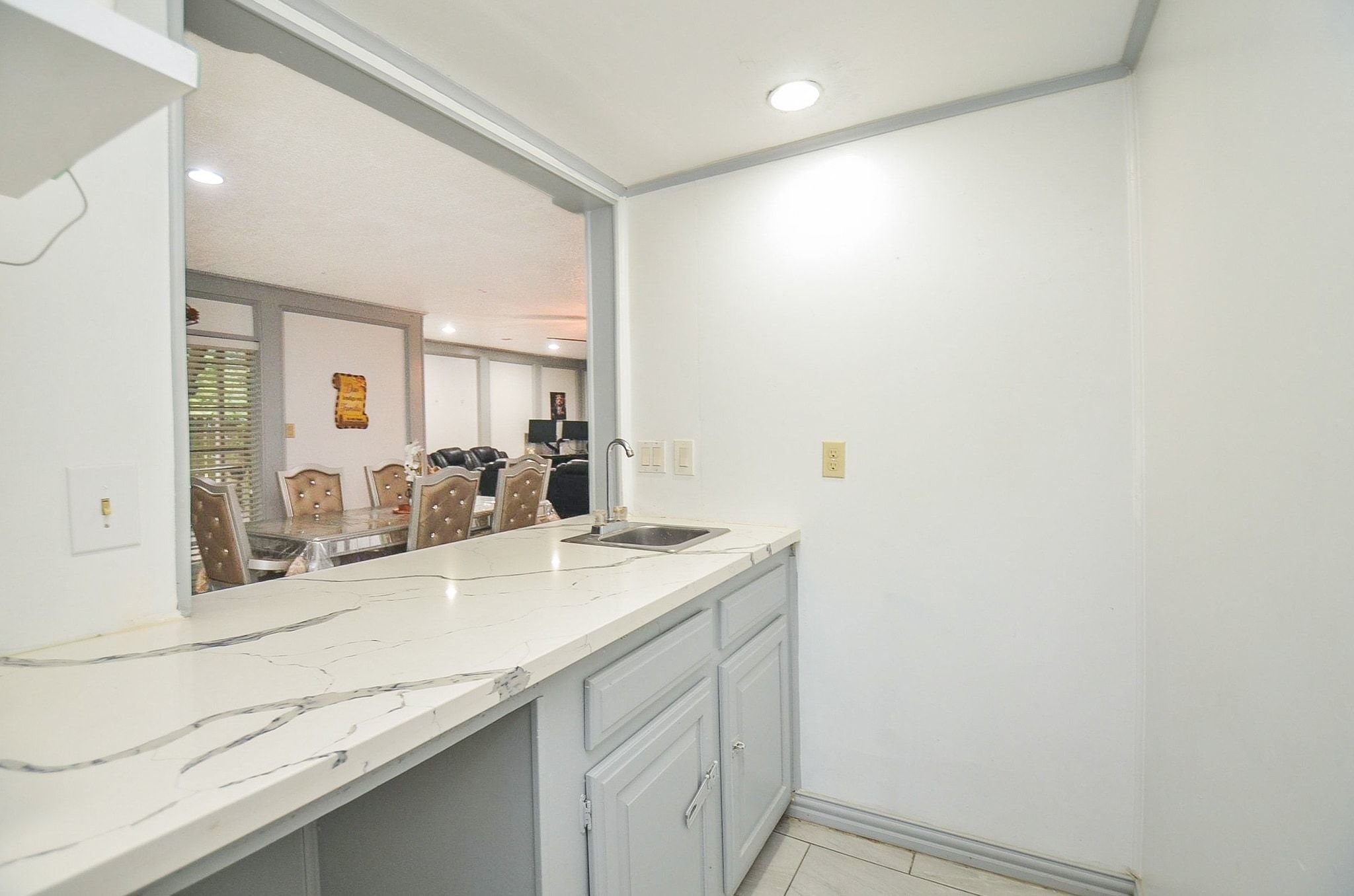Notice this tucked away dry bar with elegant marbled countertops, custom cabinetry, a prep sink, and a pass-through window overlooking the main living area.