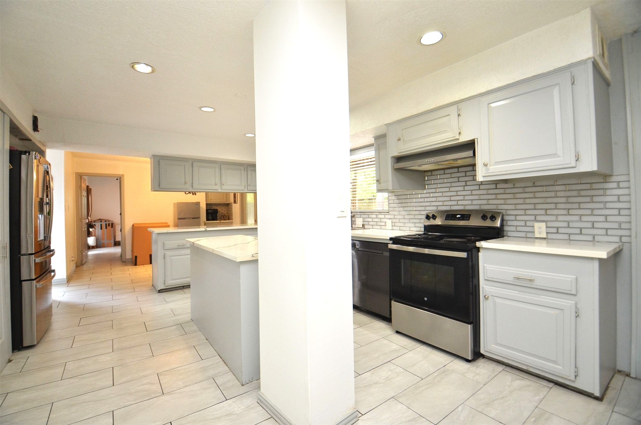 Open kitchen with quartz island, gray cabinets, subway backsplash, stainless appliances, and tile floorsopens to dining/living.