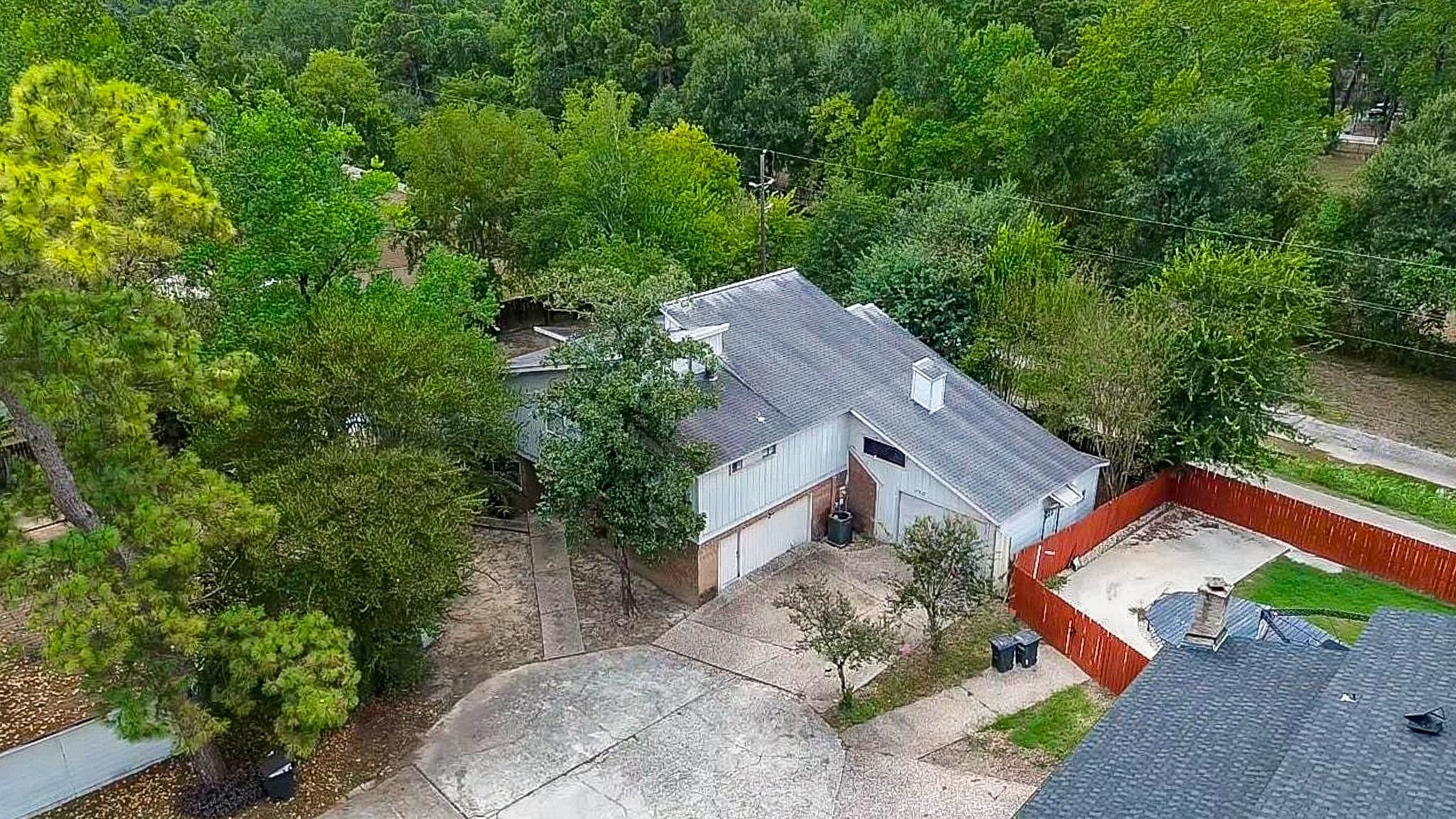 Aerial perspective highlighting the spacious, mature-tree setting, long driveway, and multi-bay garage with fenced side yard.