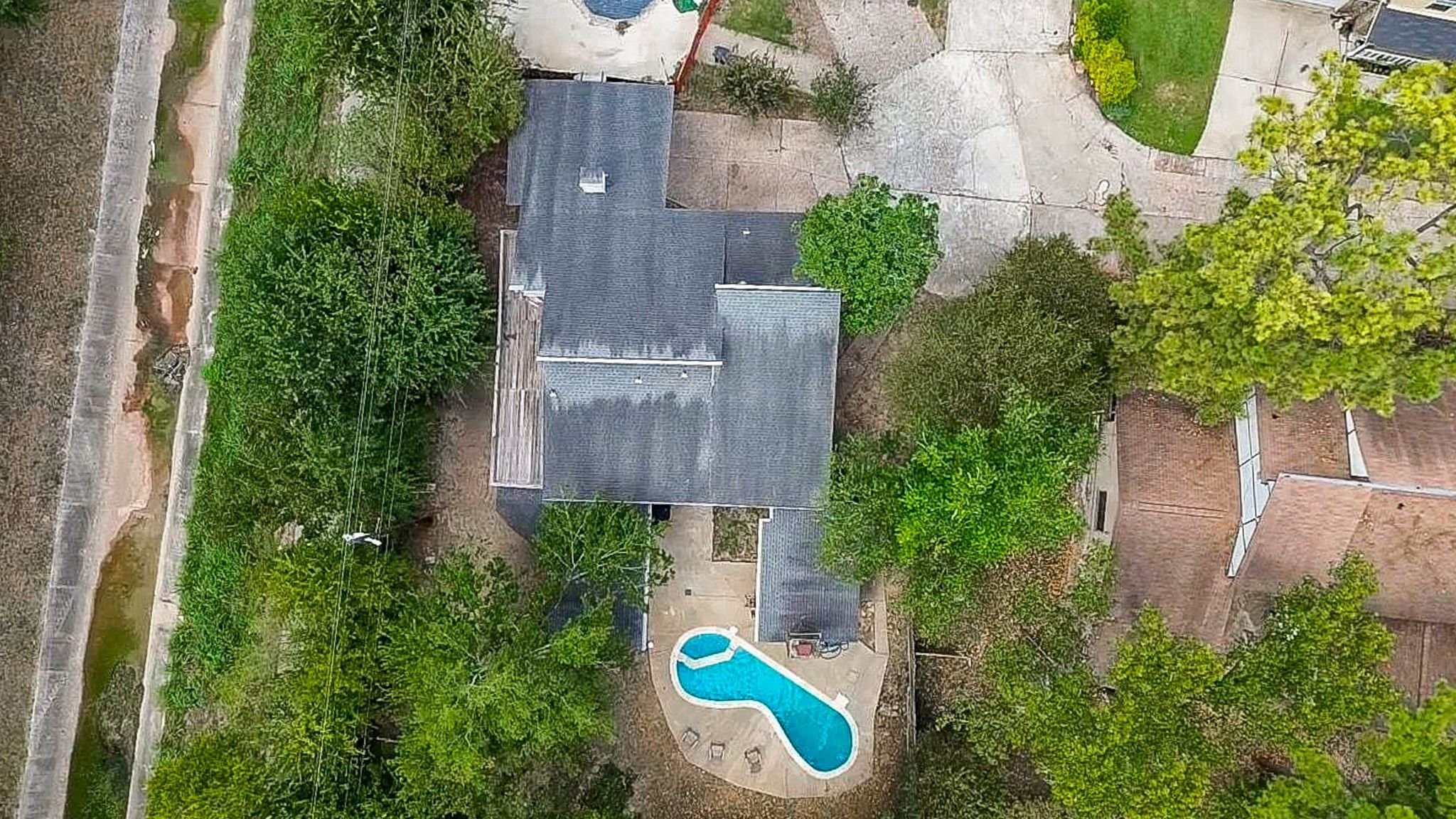Aerial view of the property showcasing the oversized, tree-shaded lot, extra-long driveway with ample parking, multiple garage bays, and a fenced side yard.