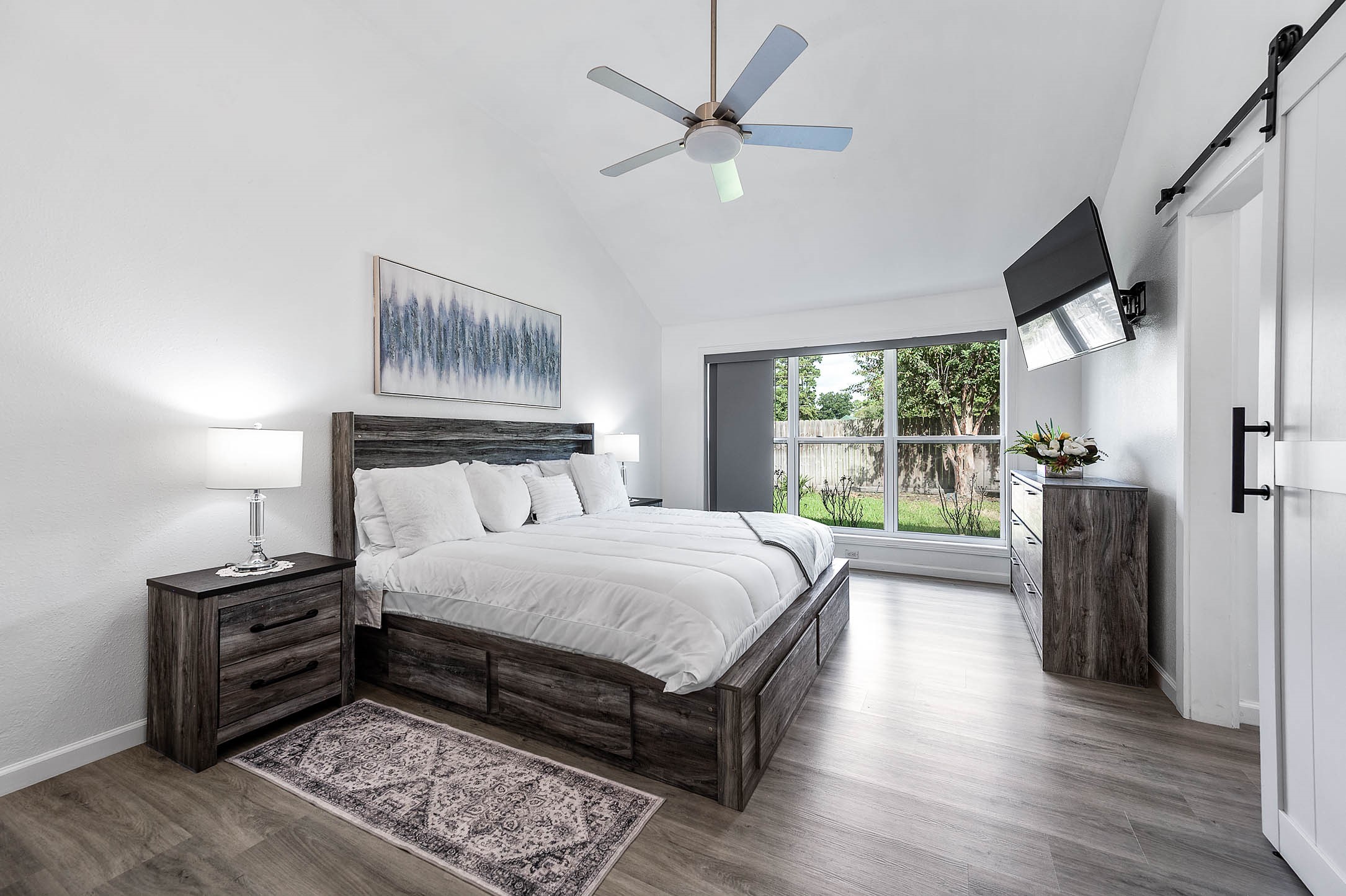 This primary suite greets you with
high ceilings, ceiling fan with lighting,
and large windows with blinds
allowing in natural light to brighten up
this spacious primary bedroom.