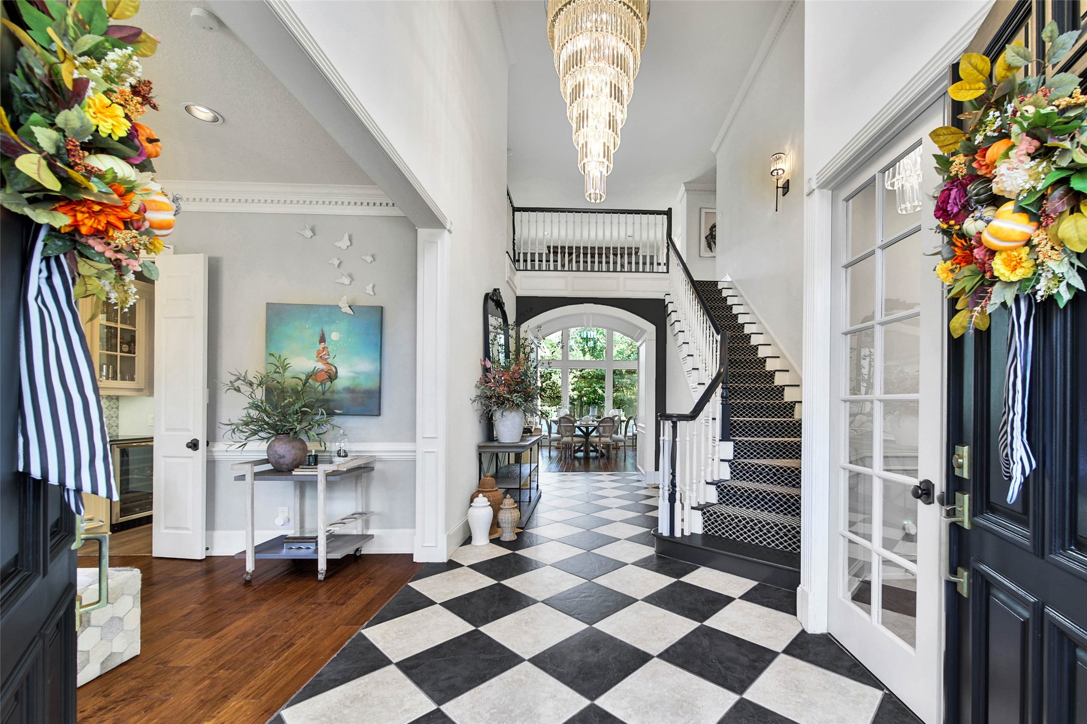 Stunning entryway featuring elegant black and white checkered flooring, a grand chandelier, and a striking staircase leading to the second floor. Decorative accents and abundant natural light create a welcoming ambiance.