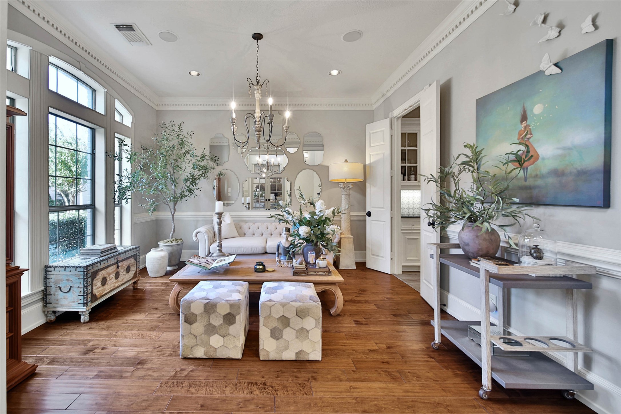 Formal living room with abundant natural light, featuring a stylish chandelier, sophisticated decor, and rich hardwood floors.