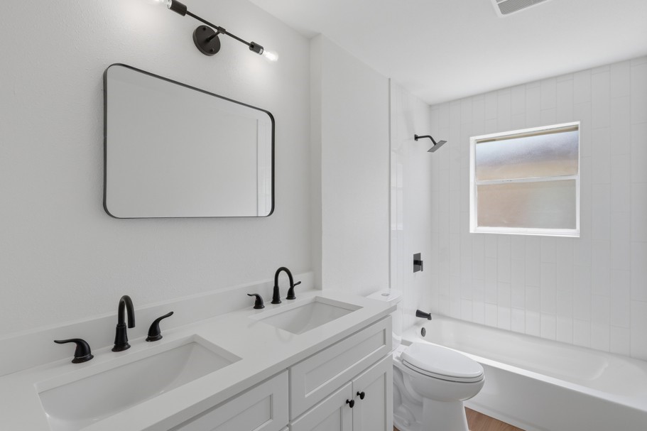 The secondary bathroom features quartz countertops, dual sinks, and classic subway tile extending to the ceiling for a polished, timeless finish. The clean and simple design creates a bright, functional space with a modern touch.